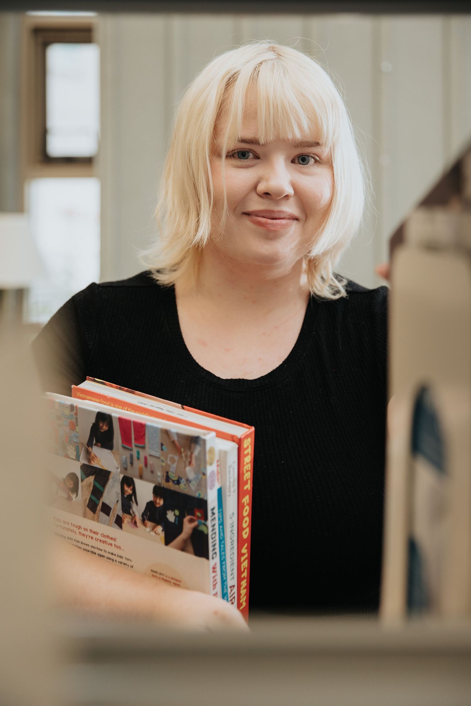 Person in black shirt browsing through books in a library setting.