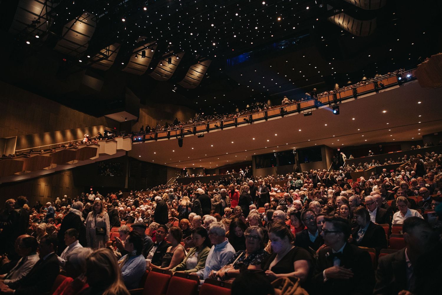 Audience seated in a dark auditorium with dramatic lighting and starry ceiling effects.