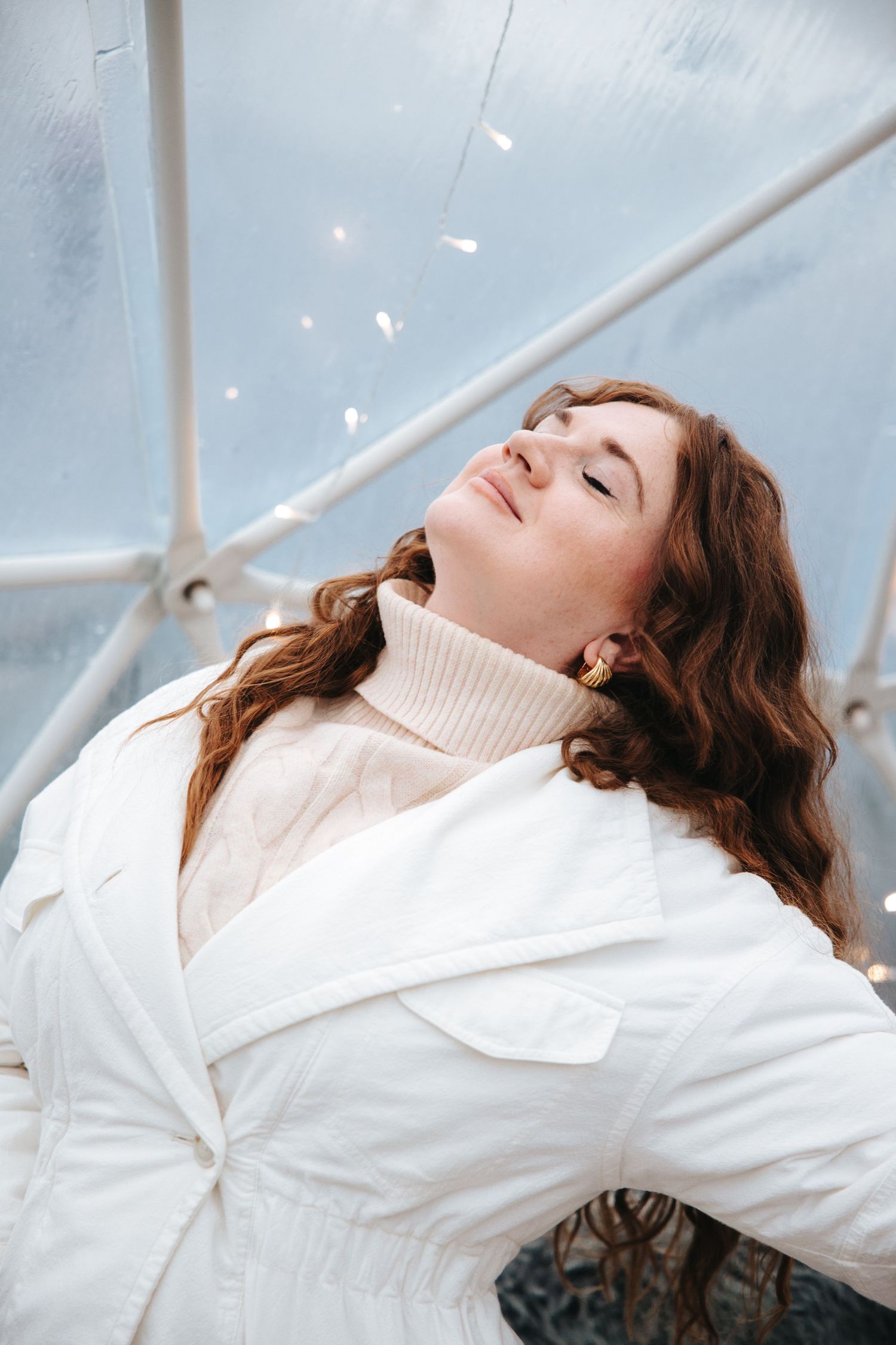 Model in white turtleneck and jacket poses against bright background in artistic photoshoot.