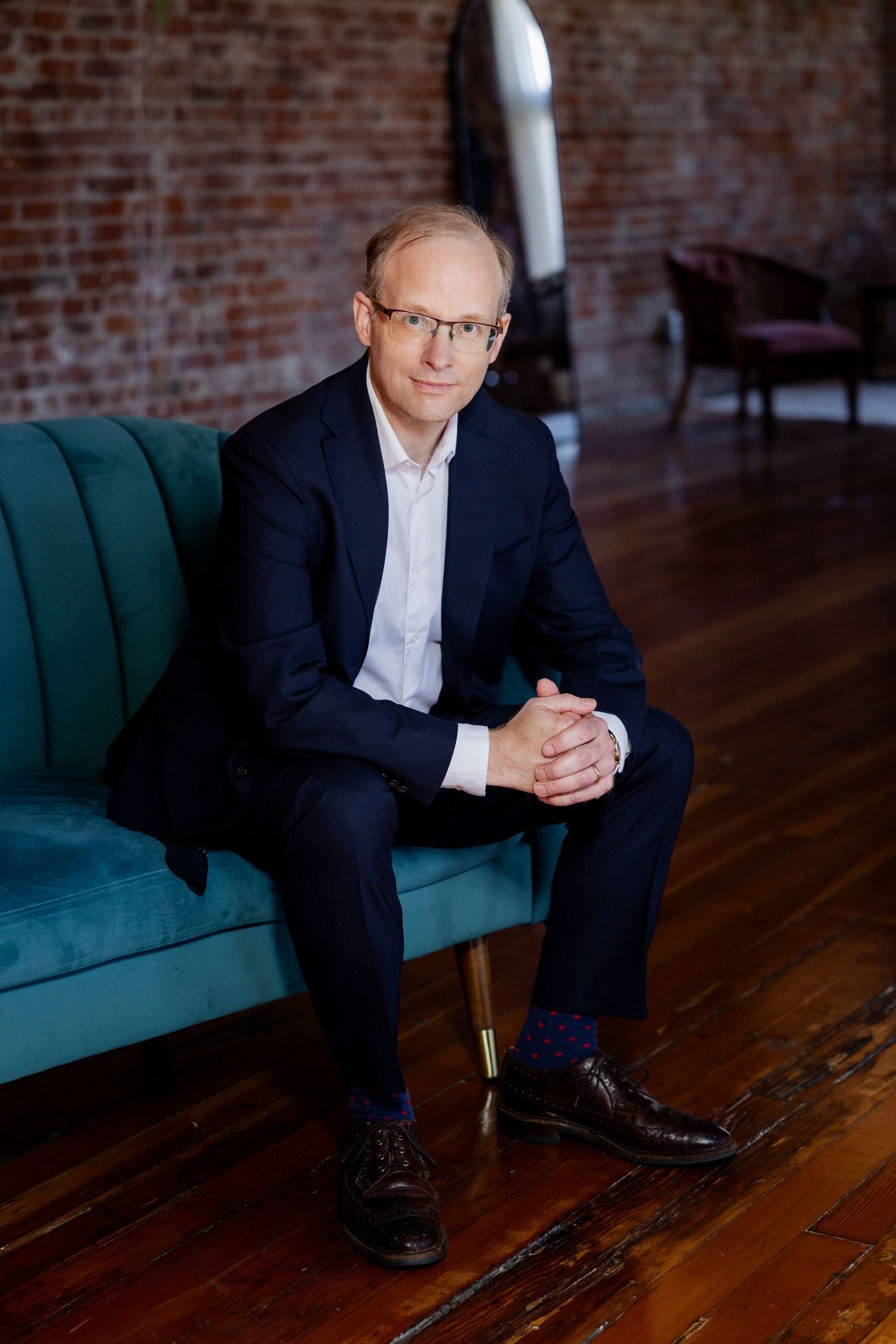 Professional seated portraits on teal couch against brick wall background.