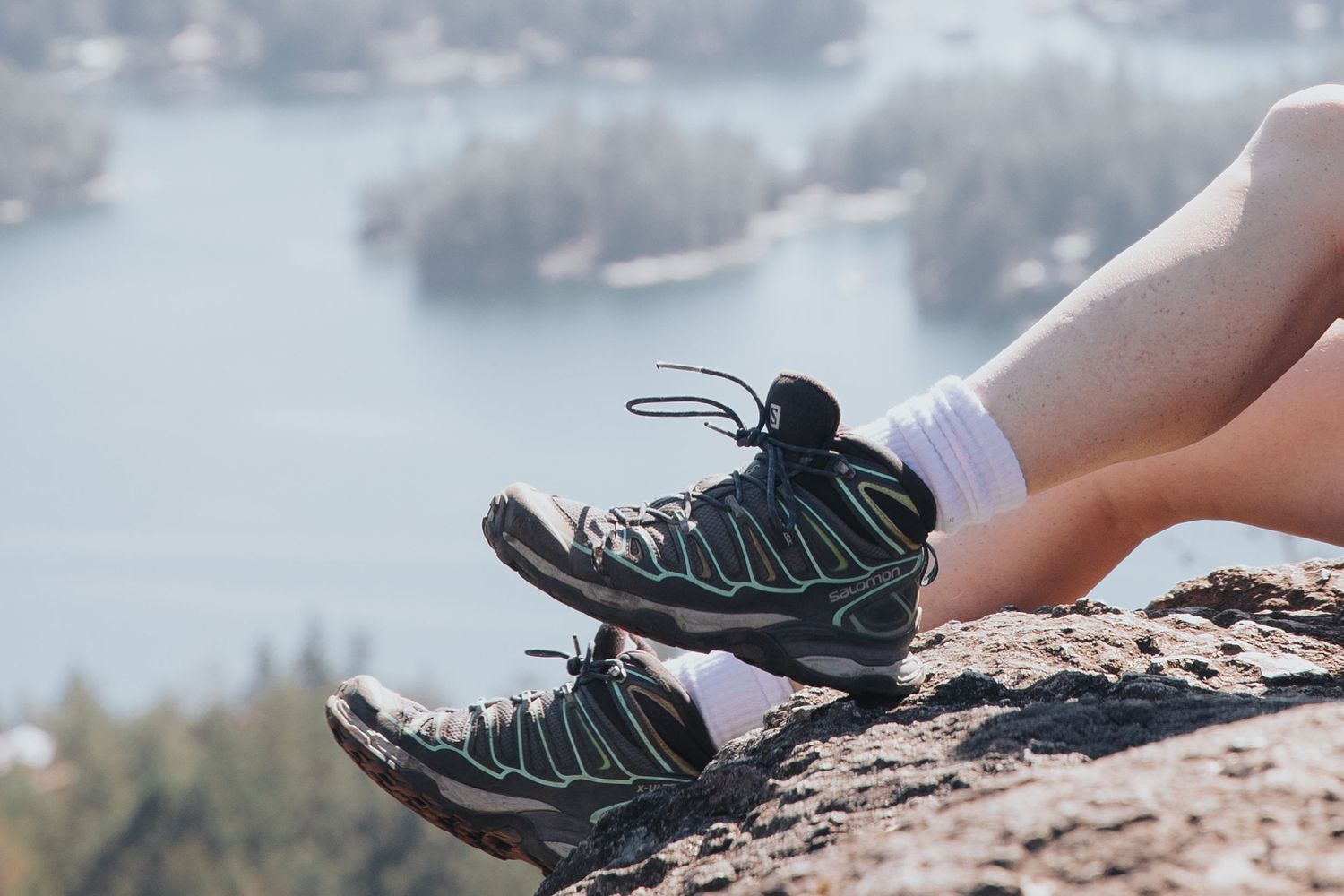 Hiking boots resting on rocky cliff edge overlooking a scenic lake view.