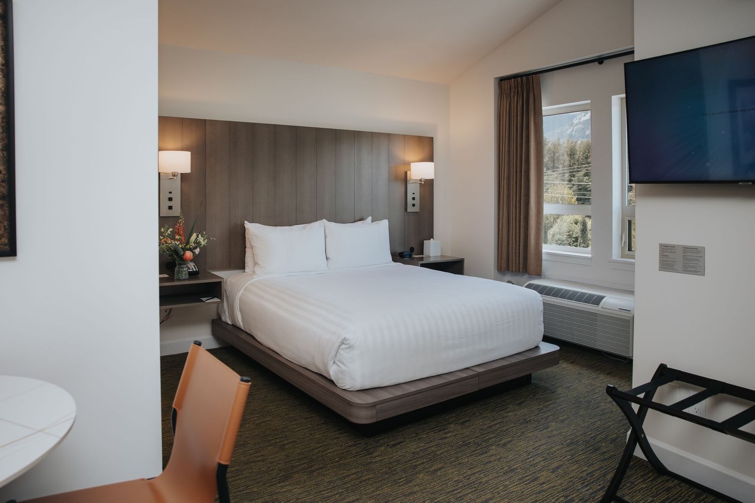 Spacious hotel suite with contemporary decor featuring white bedding and wall-mounted TV.