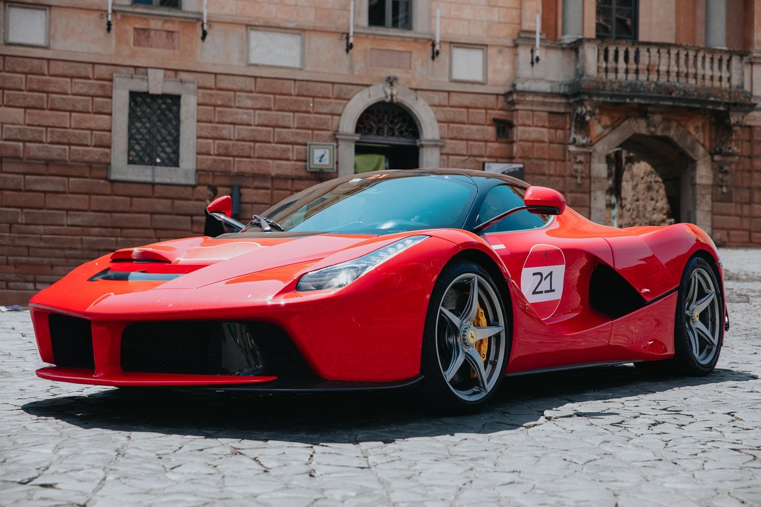 Line of red Ferrari supercars parked along a cobblestone street.