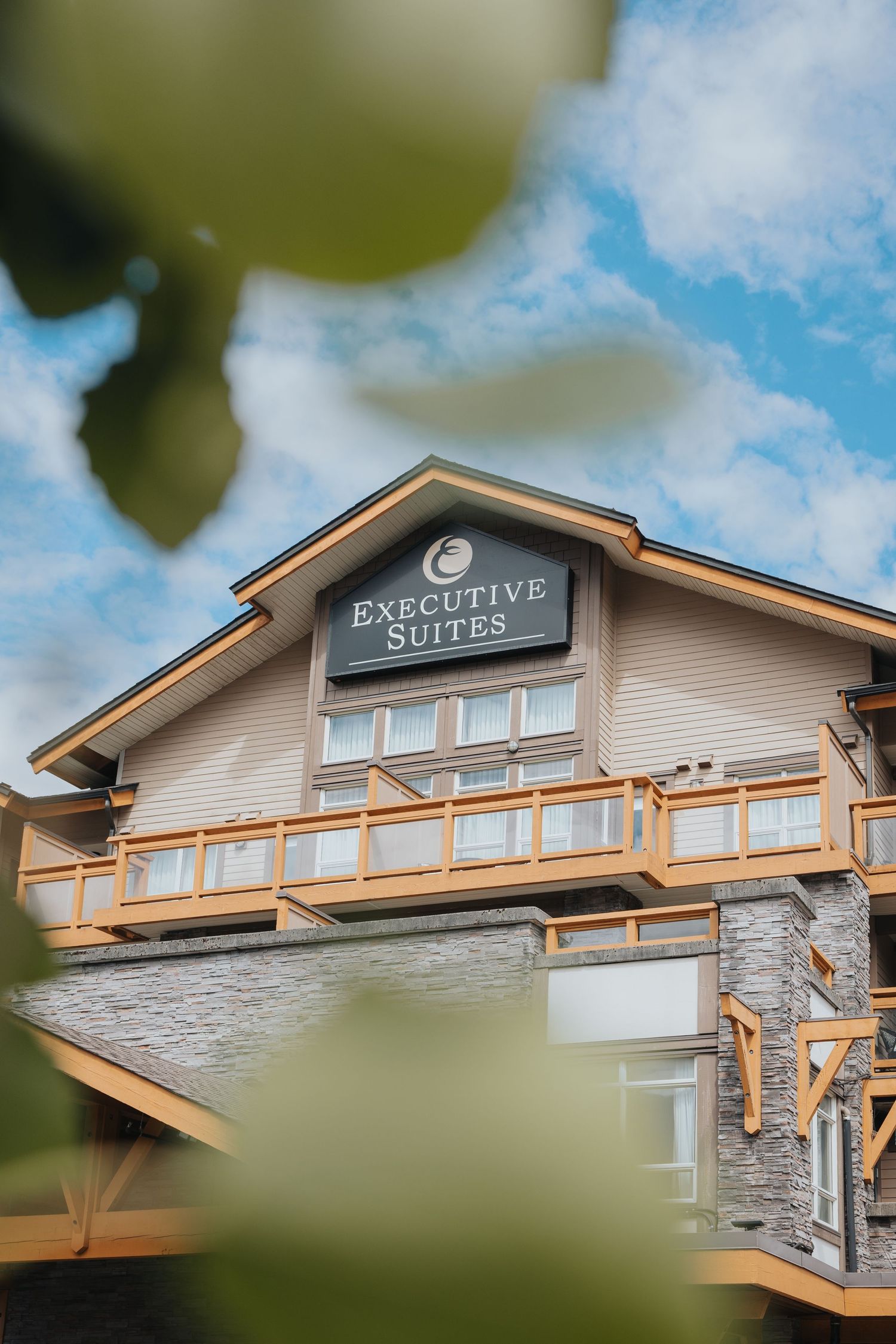 Modern executive suites building exterior with stone accents and wooden beams against blue sky.