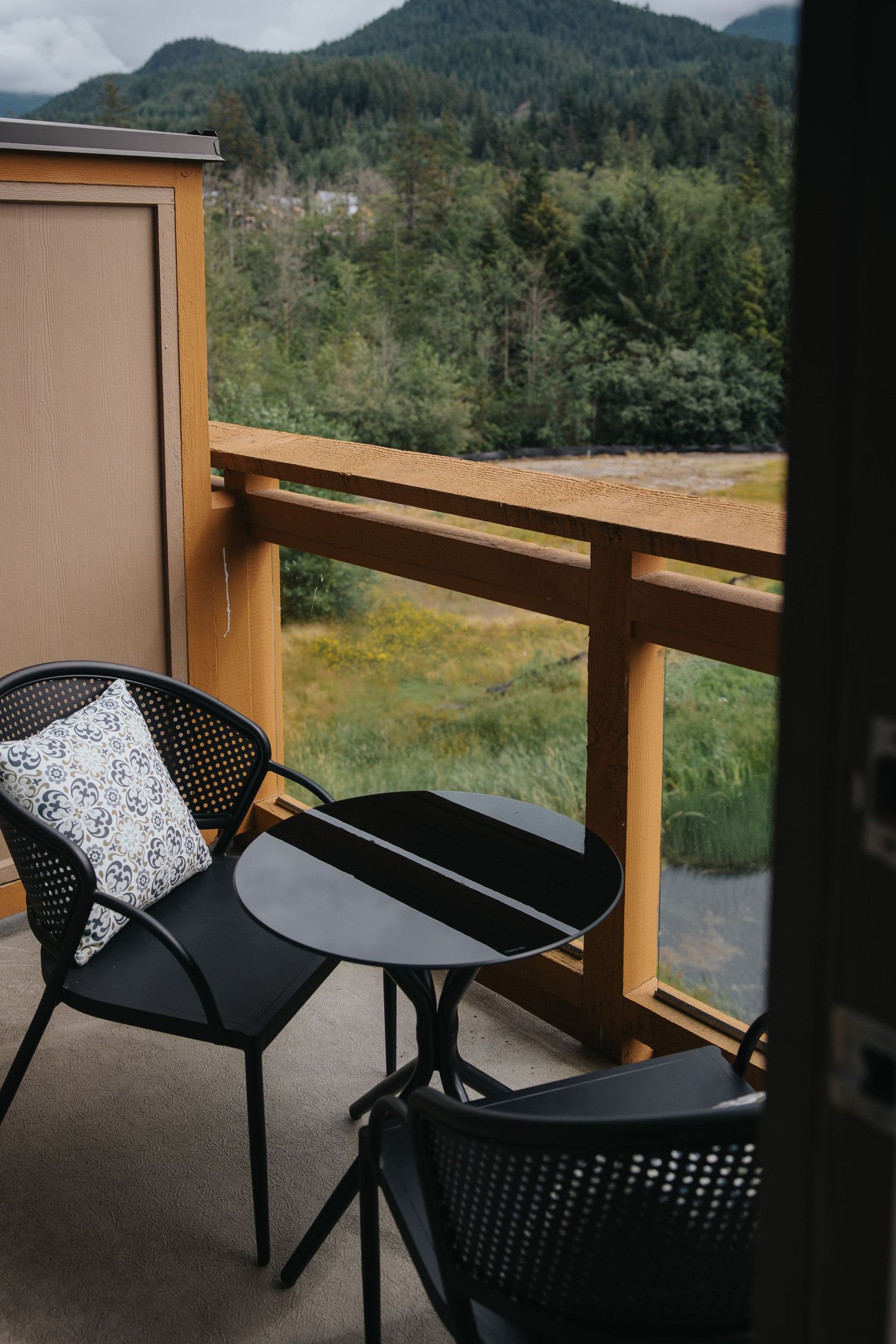 Black patio chairs with decorative cushions on balcony overlooking mountain landscape.