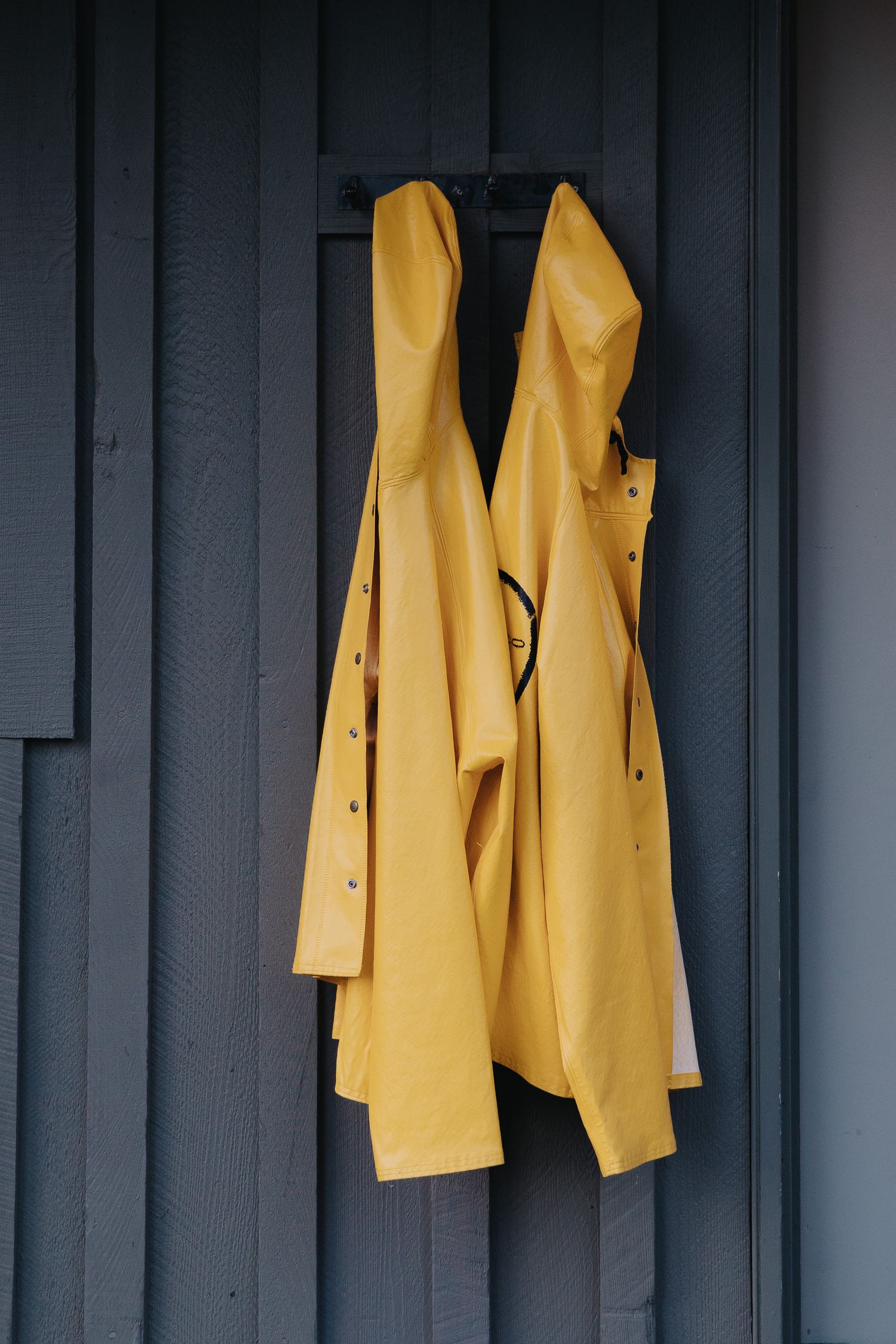 Yellow raincoats hanging on dark gray wall panels creating striking visual contrast.