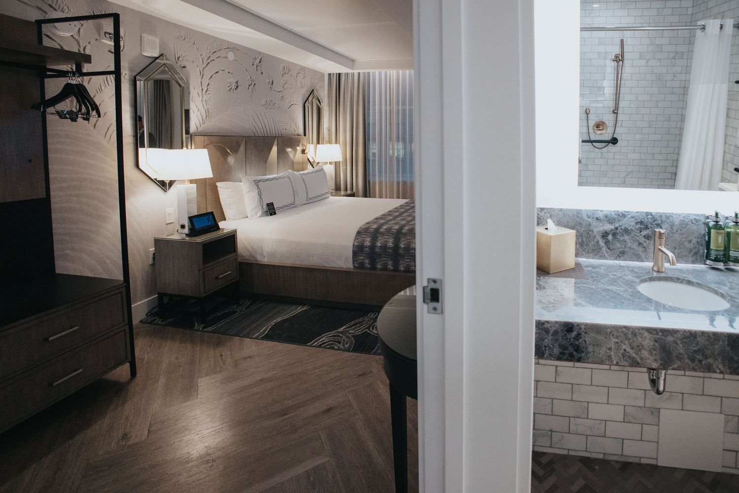 Modern hotel room interior with white bedding, grey accents, and contemporary furnishings.