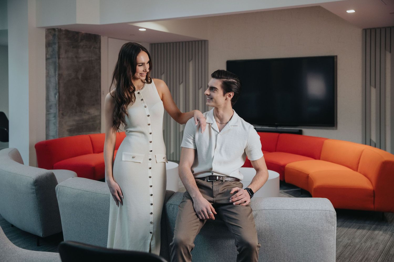 Couple relaxing on a modern gray couch in a contemporary living room with orange accents.