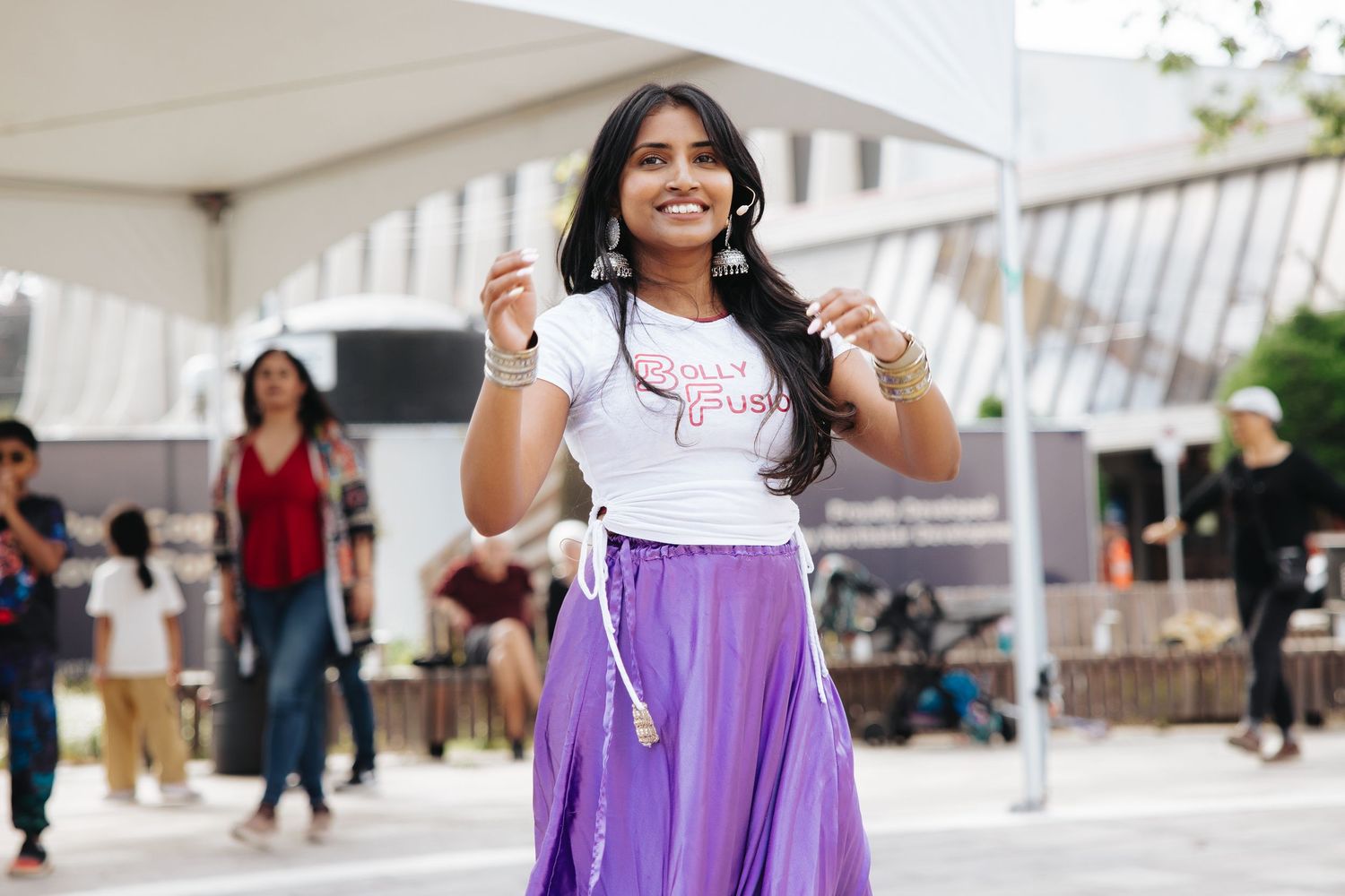 Woman in purple skirt and white t-shirt smiling at outdoor event.