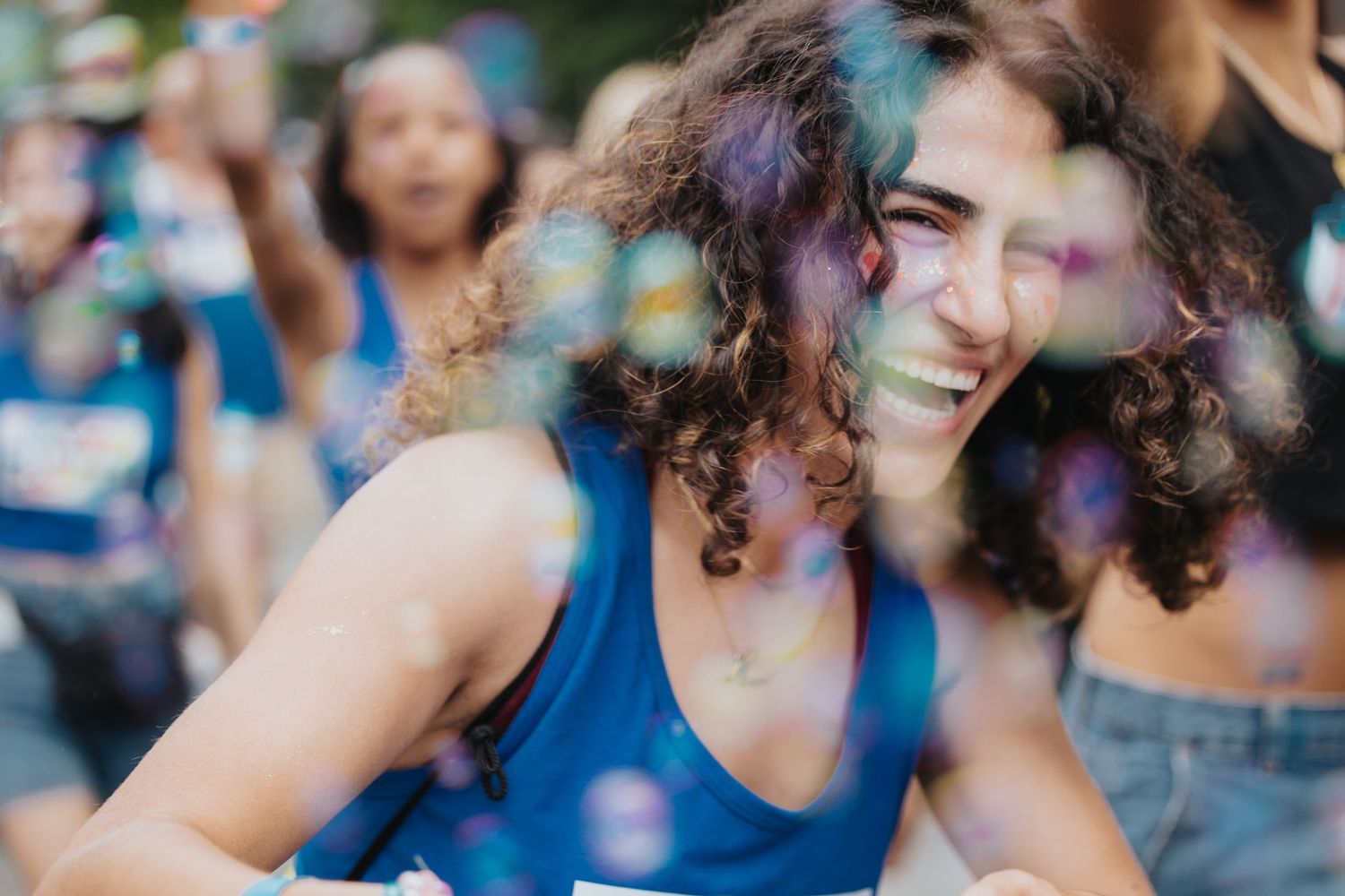 Person with curly hair laughing joyfully at outdoor festival.