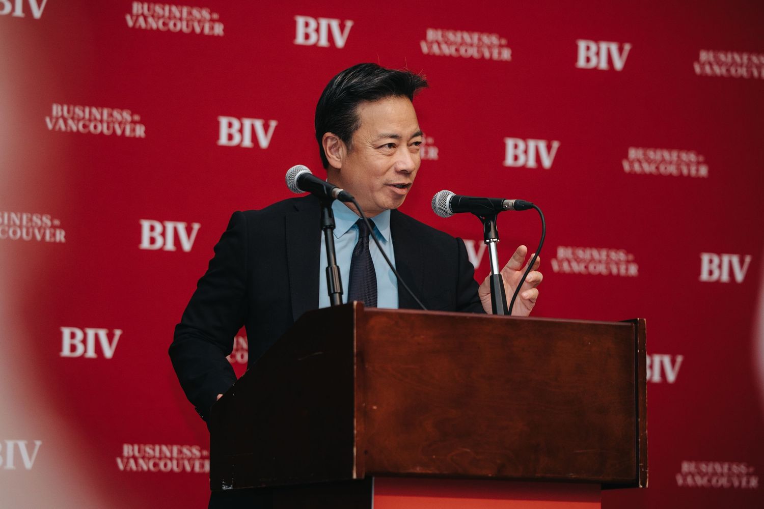 Speaker at podium giving presentation in front of red backdrop with BIV branding.
