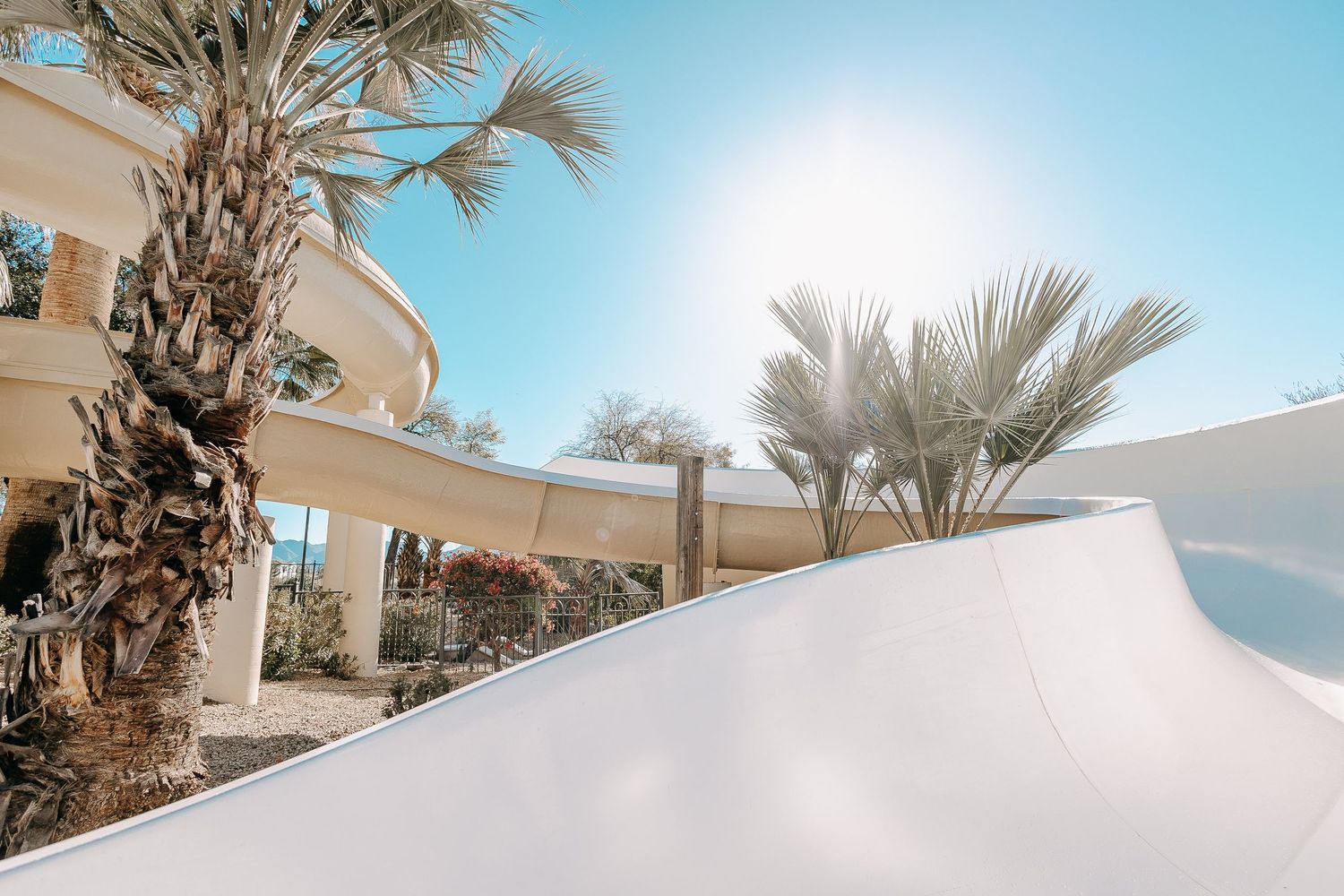 Modern white resort architecture with palm trees against bright blue sky.