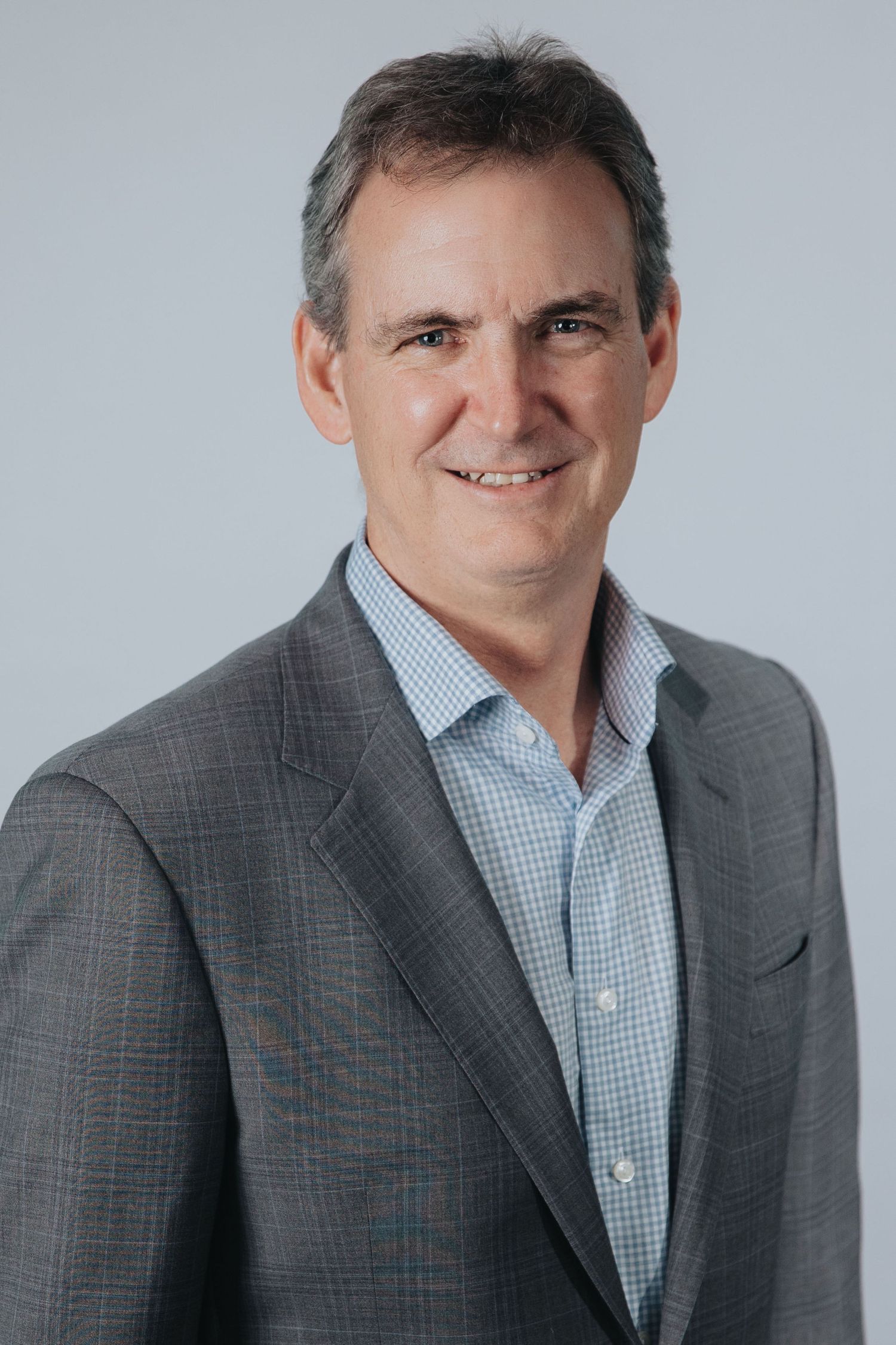 Professional headshot series of person in gray suit and checkered shirt against light background.