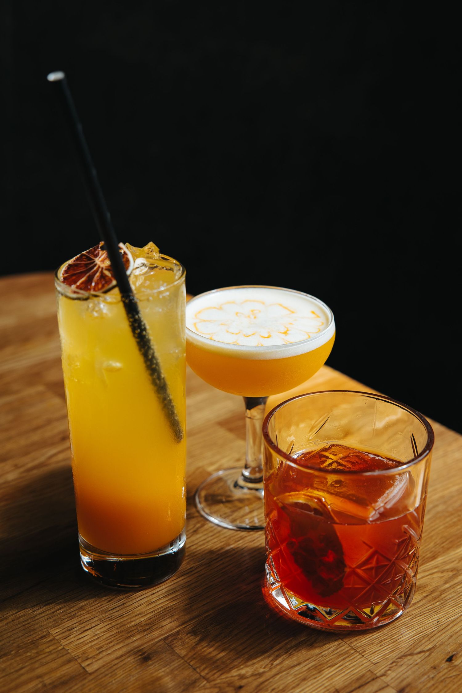 Assorted colorful cocktails arranged on a wooden bar top with garnishes.