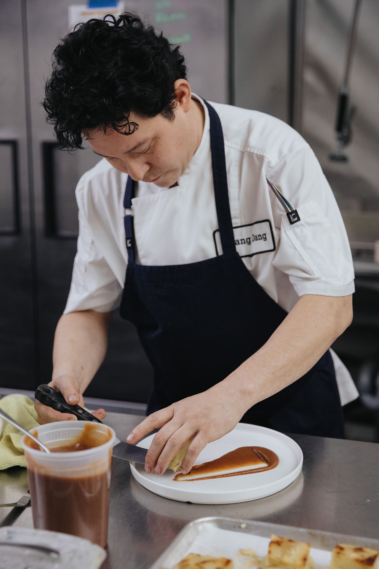 Chef in white coat and black apron carefully plates dishes in commercial kitchen.
