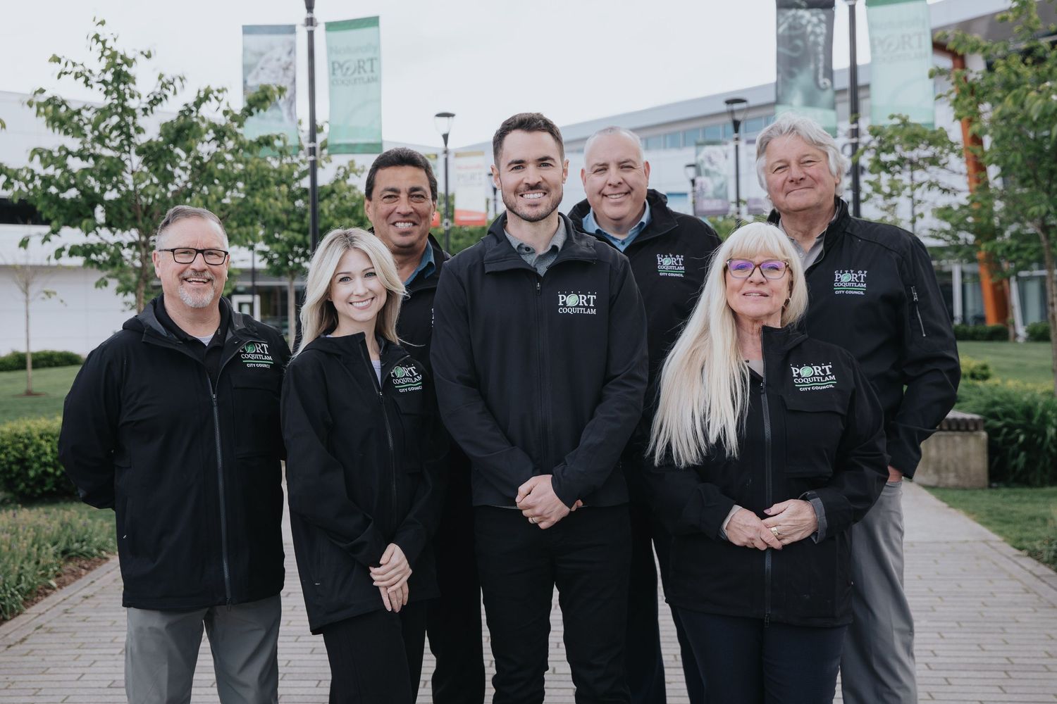 Team photo of people wearing matching black jackets standing together outdoors.