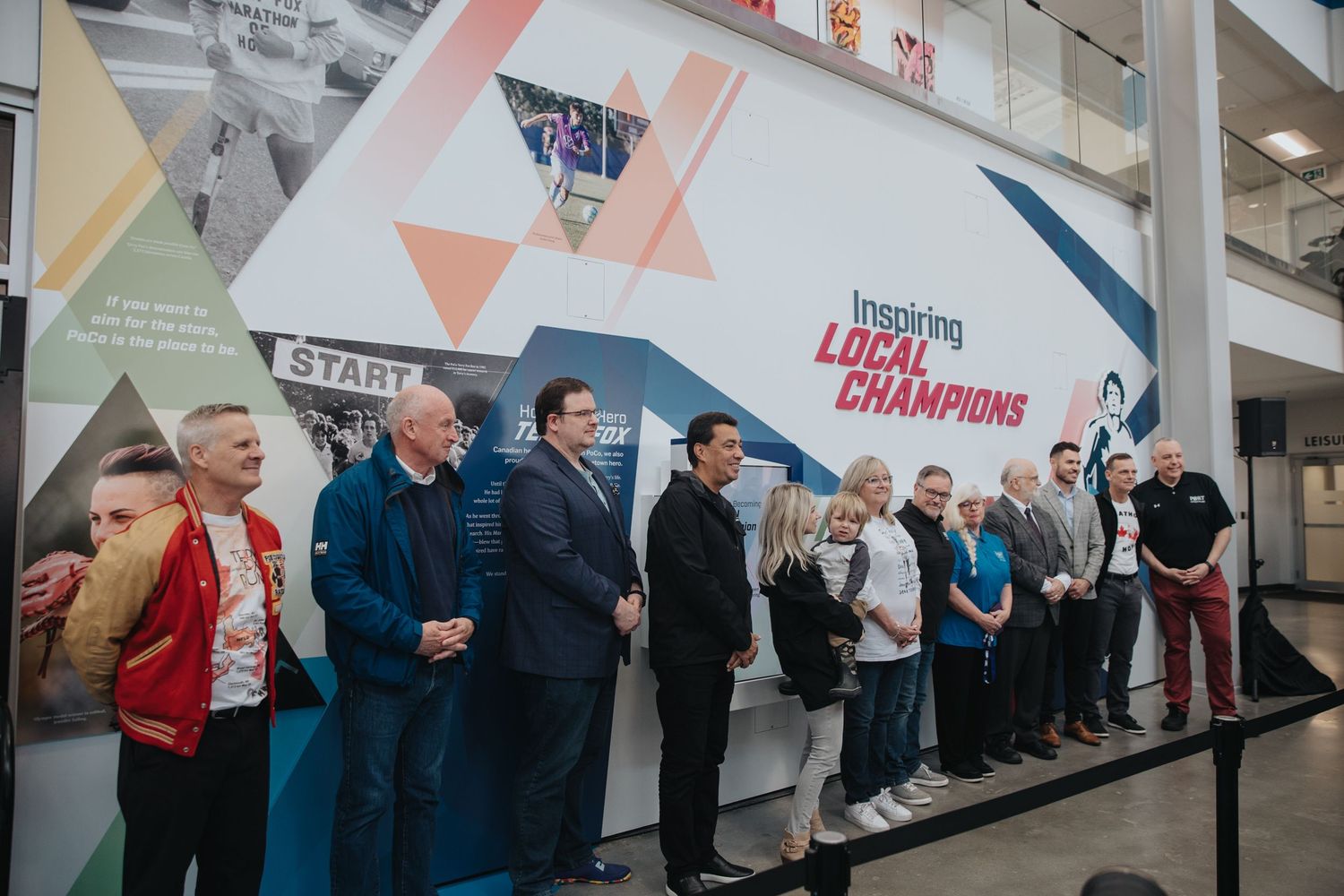 People standing in line along a wall decorated with colorful geometric shapes and banners.