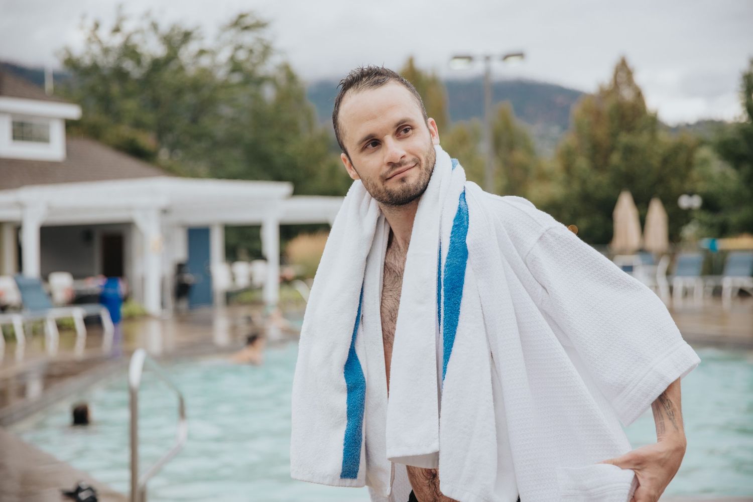 Person in white robe walking along poolside at resort.