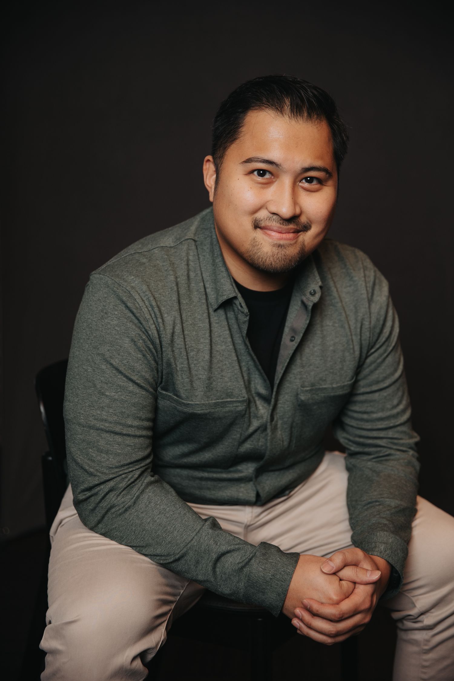 Professional headshots in grey polo showing friendly expressions against dark background.
