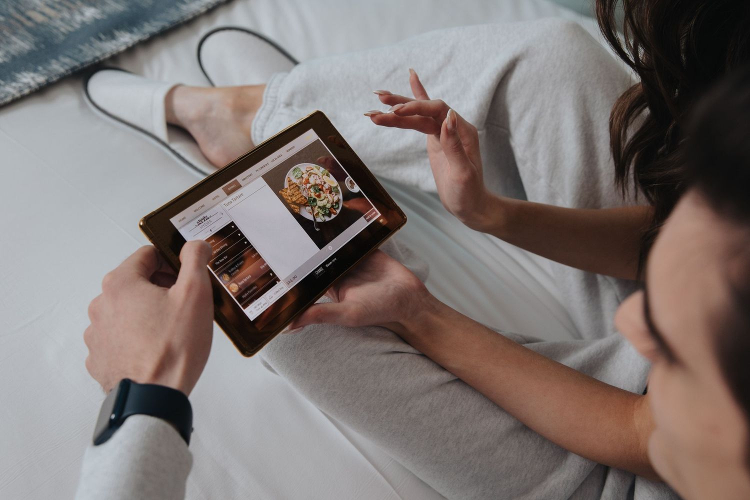 Hands holding small wooden boxes while sitting on white bedding.