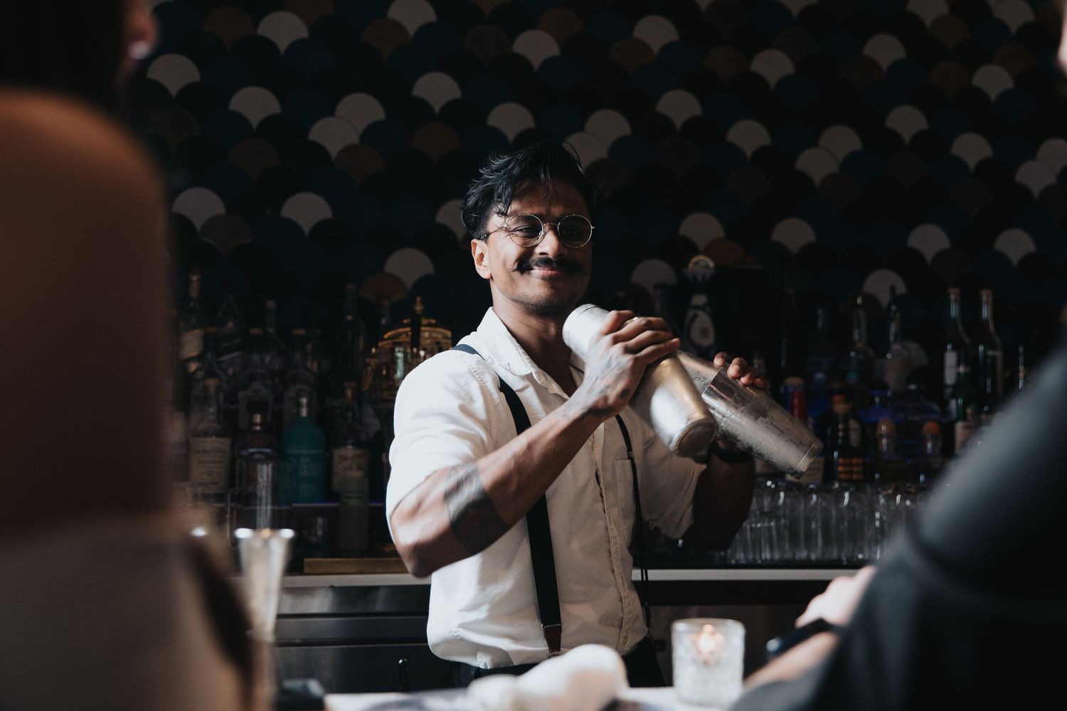 Person enjoying a drink at a dimly lit bar counter with bottles in the background.