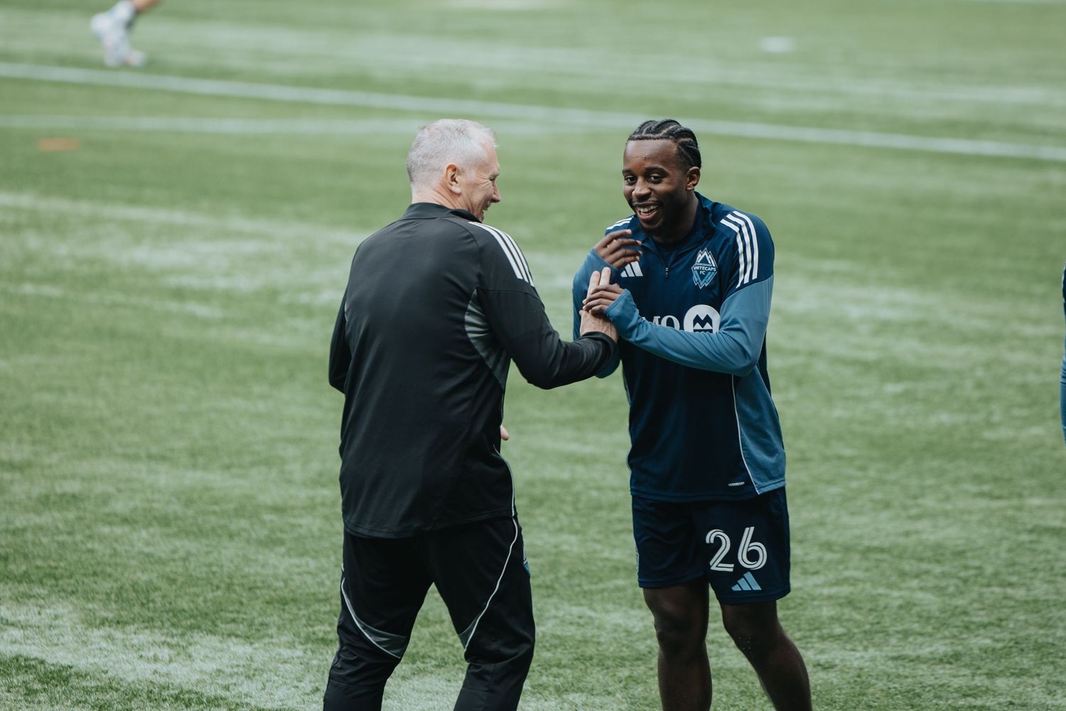 Players and staff interact on the sidelines of a soccer field during a game.