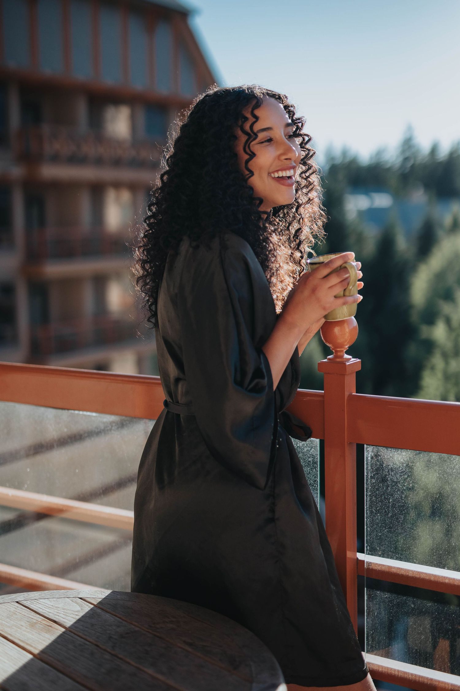 Person enjoying a beverage on a balcony overlooking mountain scenery.