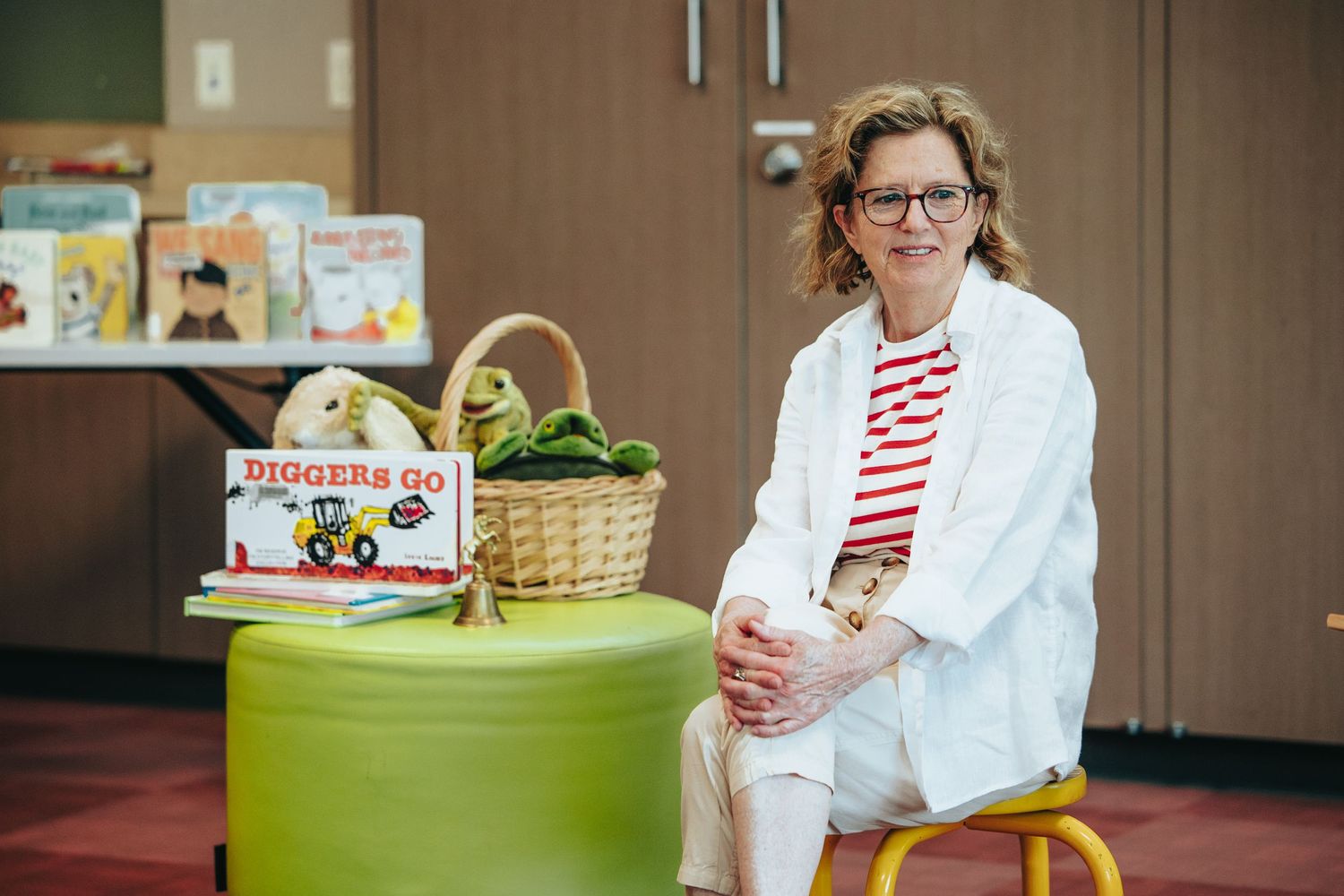 Person in white lab coat sitting on yellow stool next to basket and children's books.