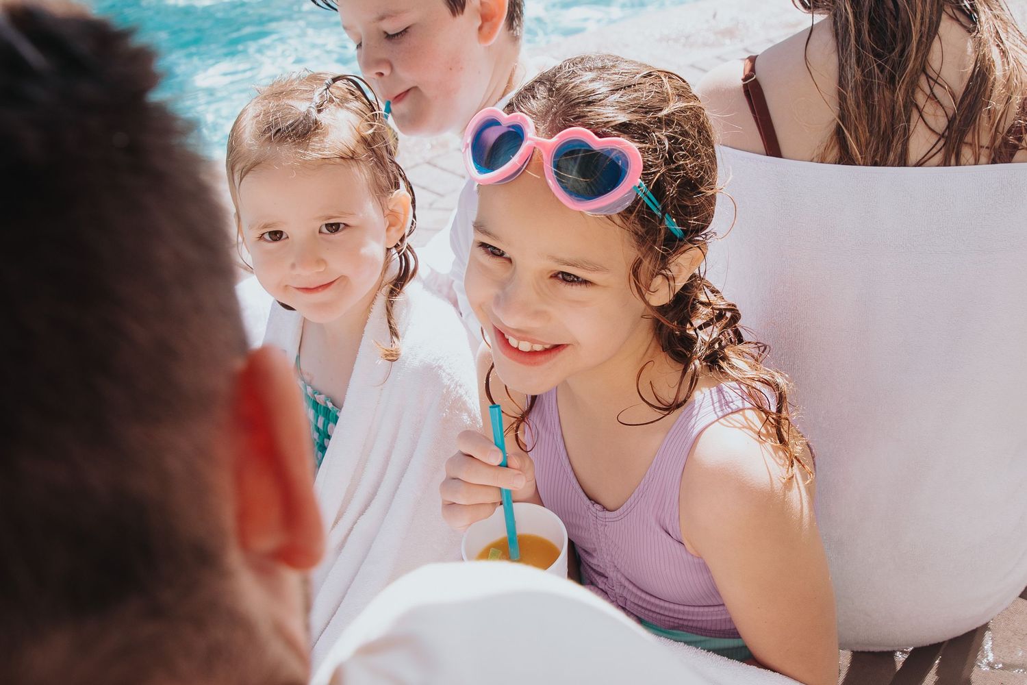 Group enjoying a sunny poolside gathering wearing colorful swimwear.