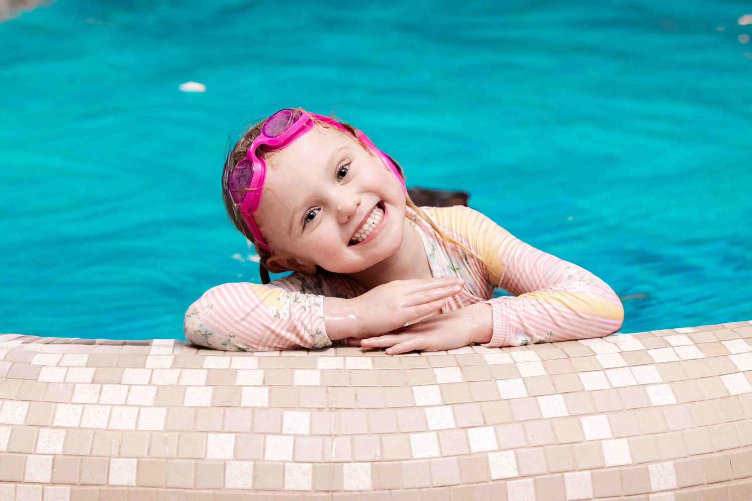 Happy swimmer in pink cap resting at pool edge with tiled border.