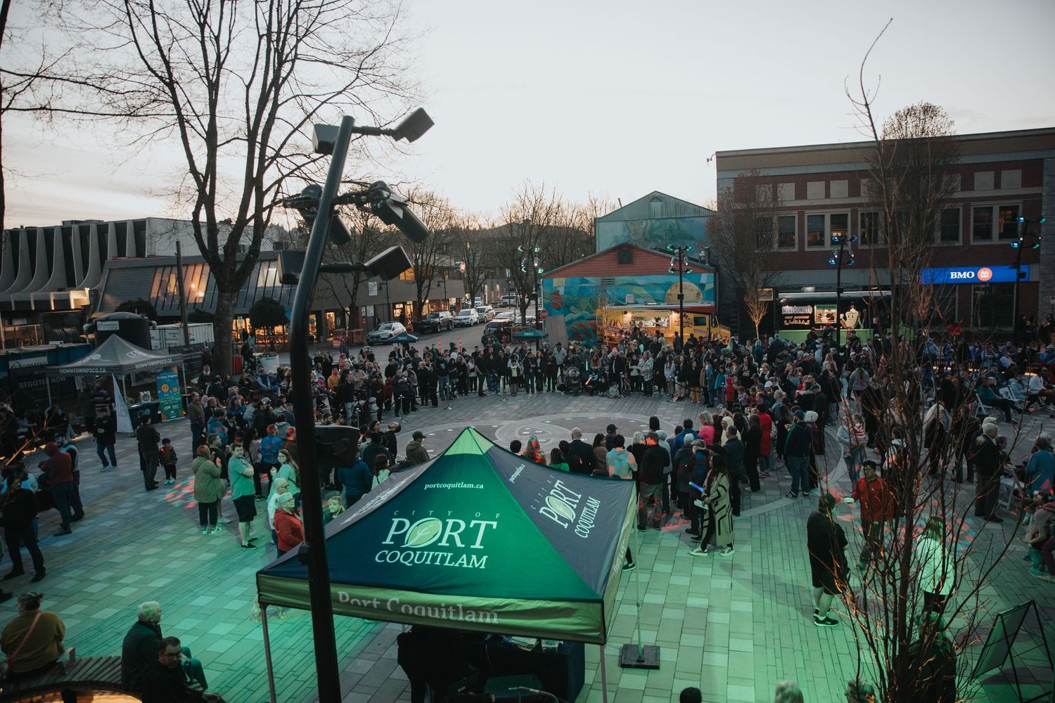 Panoramic view of outdoor event space with green tents and crowd at dusk.