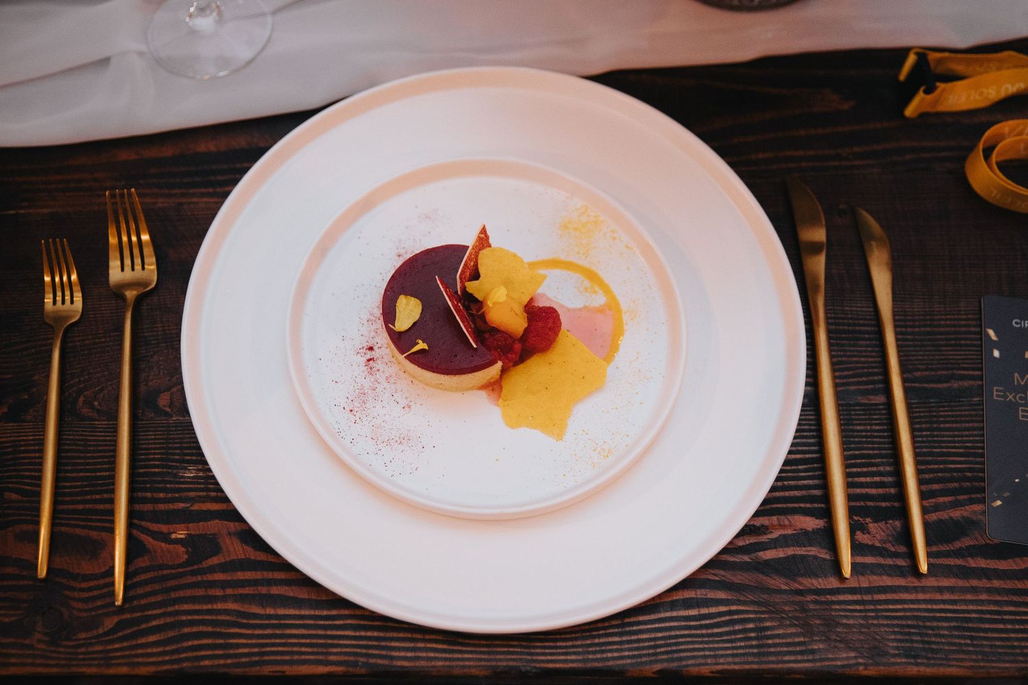 Elegant table setting with white plates and gold cutlery on dark wood surface.