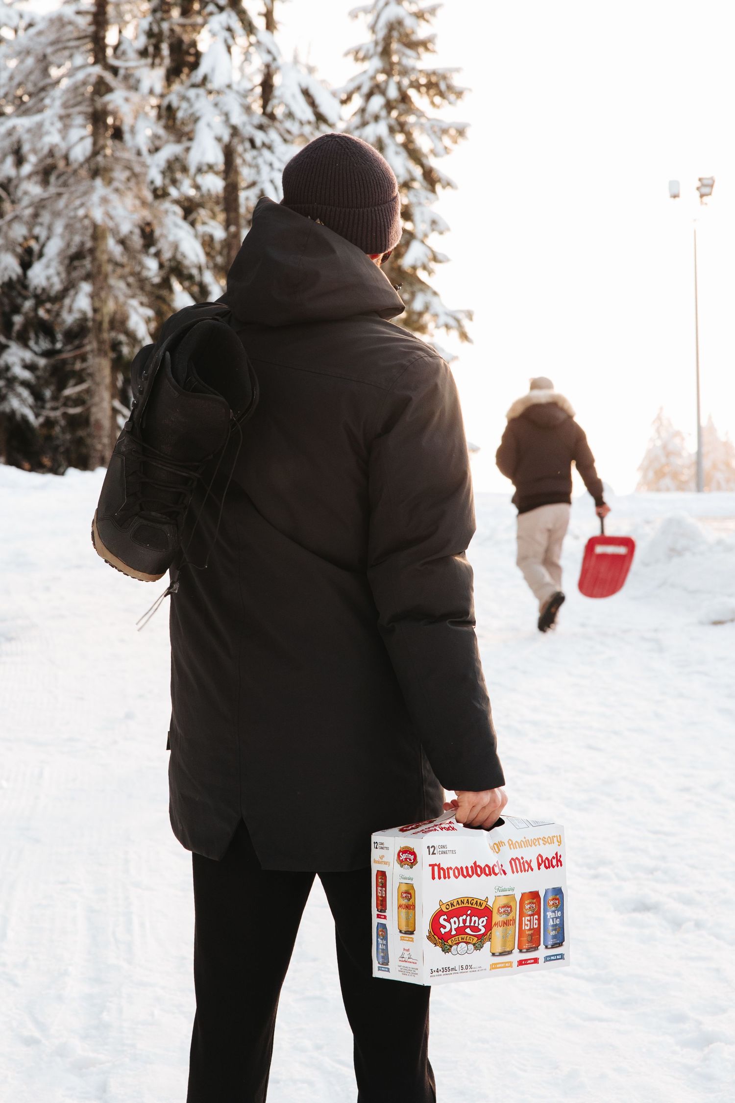 Someone walking through snow carrying a case of Spring Brewery's Throwback Mix Pack.