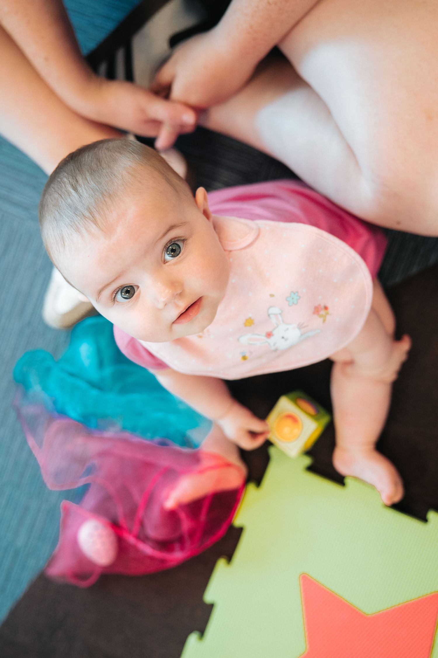Baby in pink outfit playing with colorful toys on foam mat.