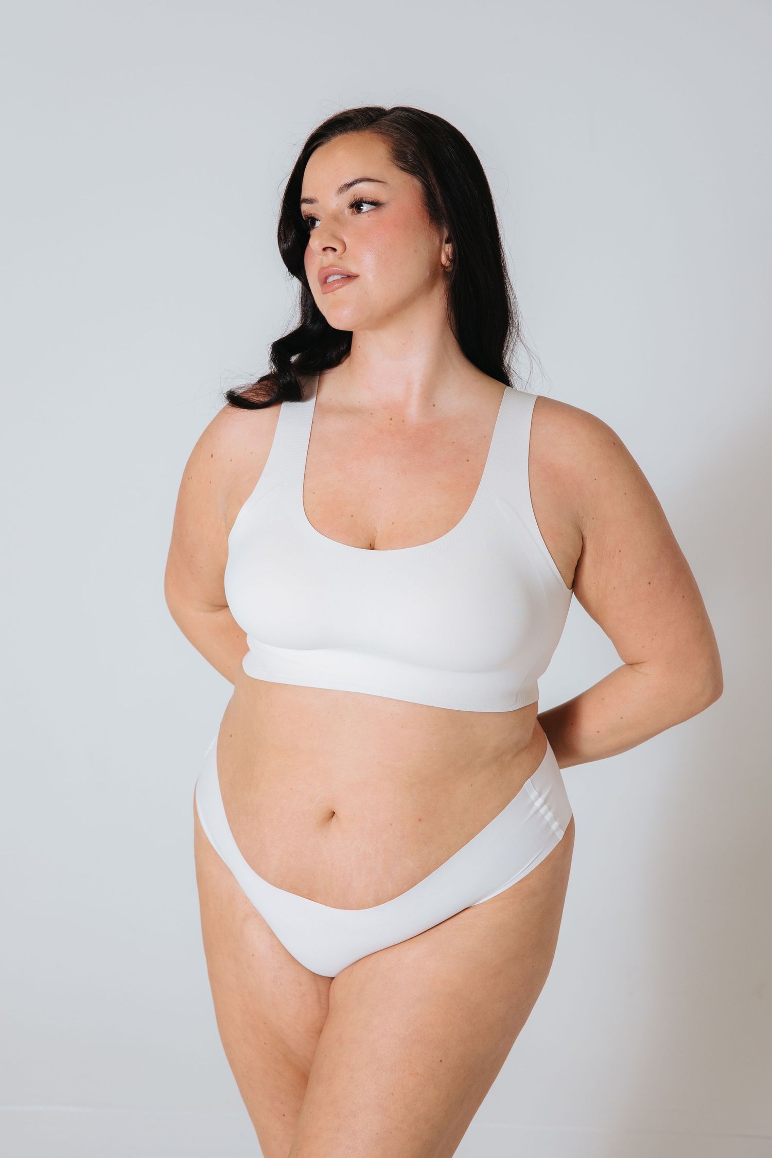 Body positive fashion photography with white lingerie against light background.