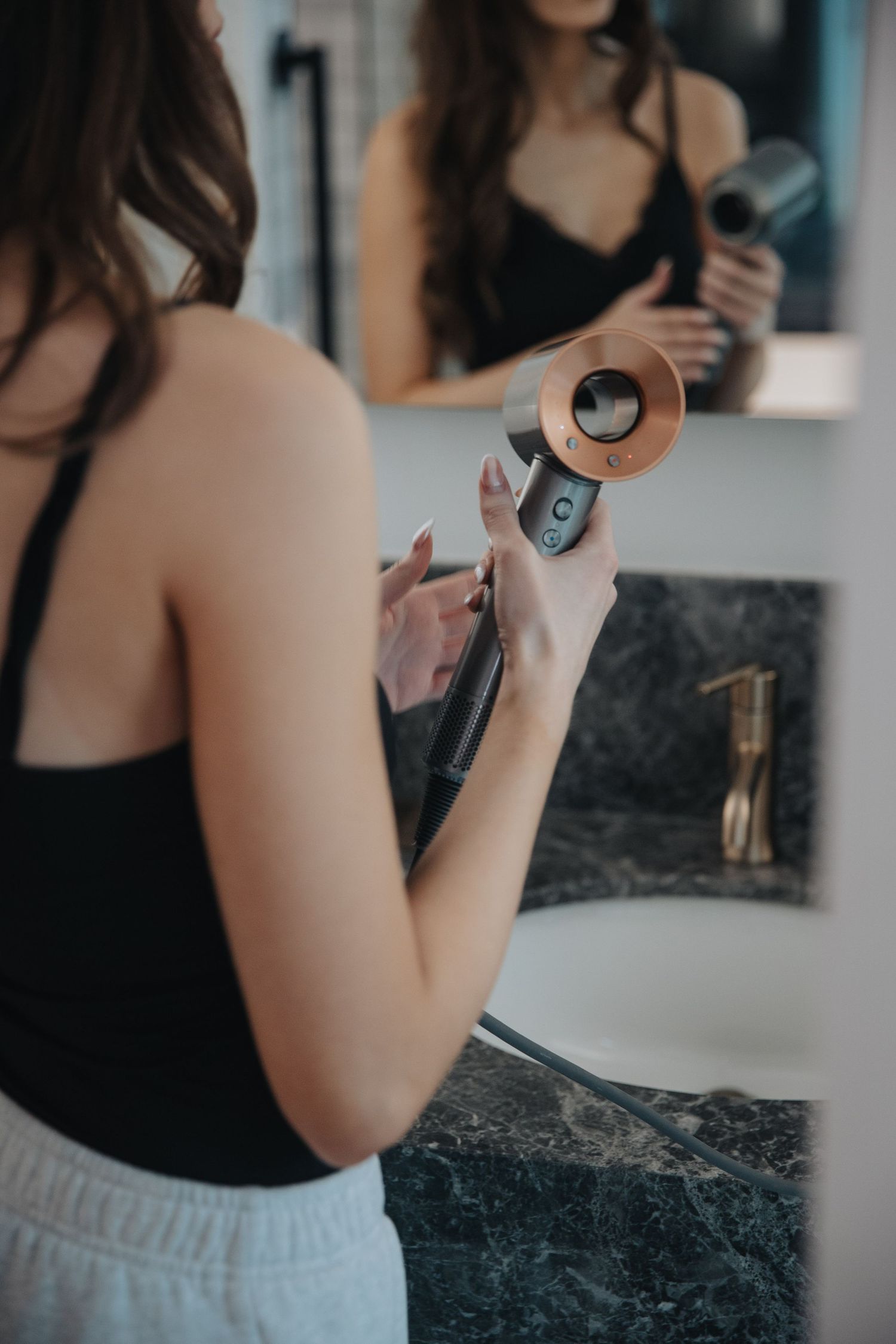 Woman in black tank top getting ready at bathroom vanity counter.