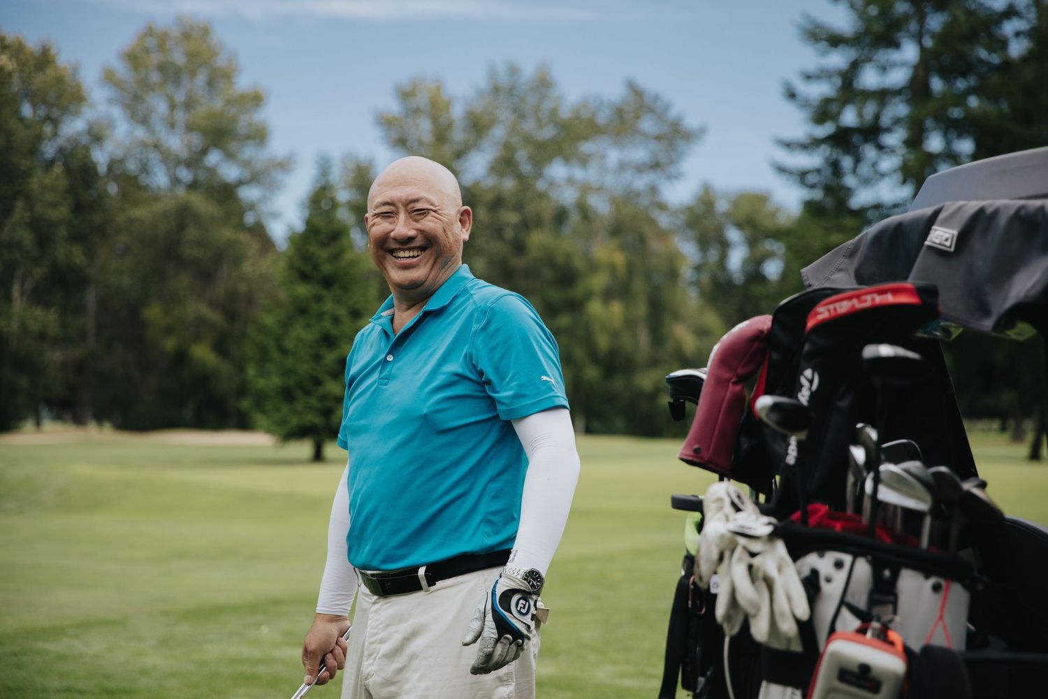 A group of golfers prepare their equipment and carts on a sunny day at the golf course.