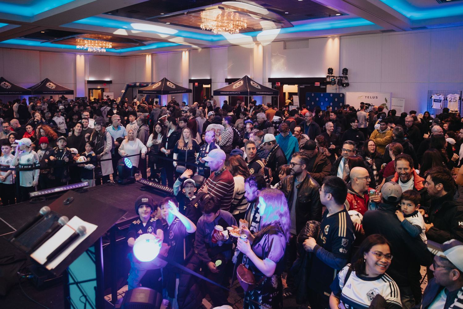 Panoramic view of a packed conference room with blue ambient lighting and multiple presentation screens.