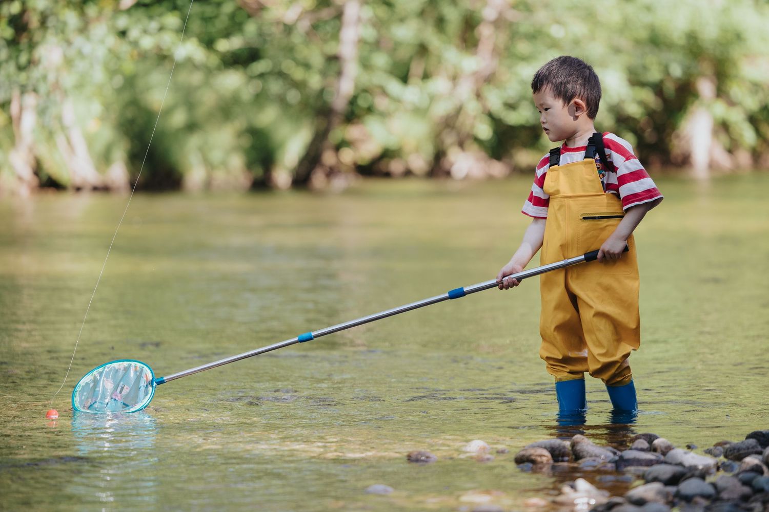 Children playing in shallow river water with nets on sunny day.
