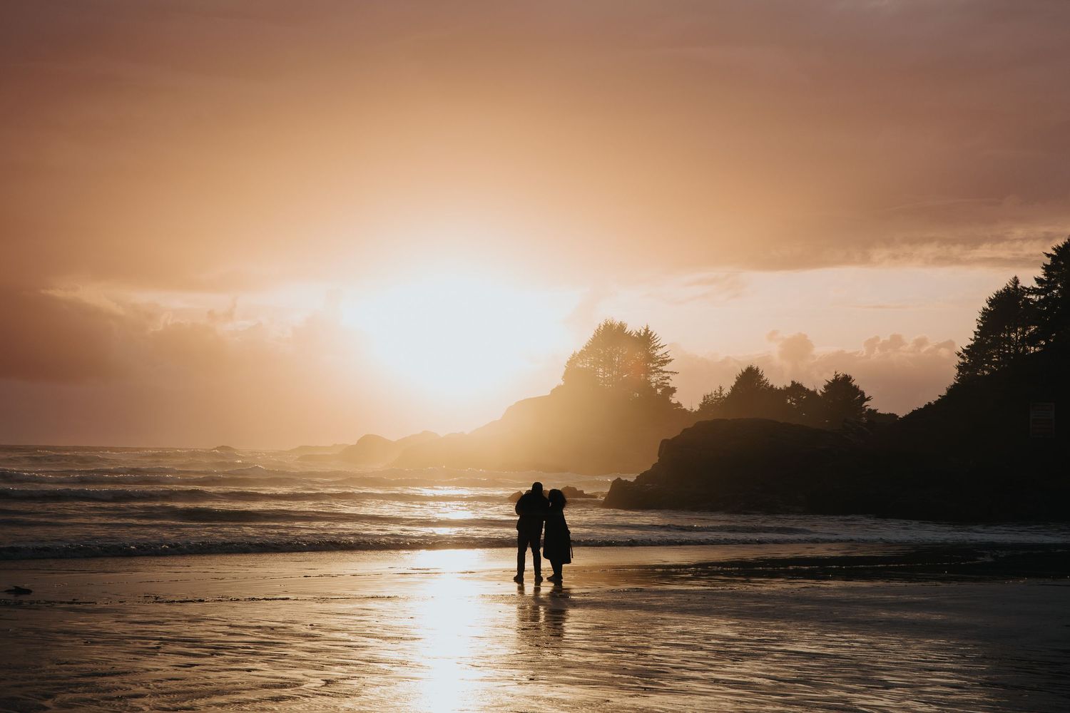 Dramatic sunset over a rocky beach coastline with silhouettes of people walking along the shore.