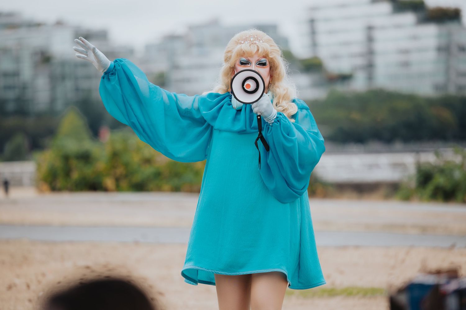 Person in turquoise sweater using megaphone outdoors.
