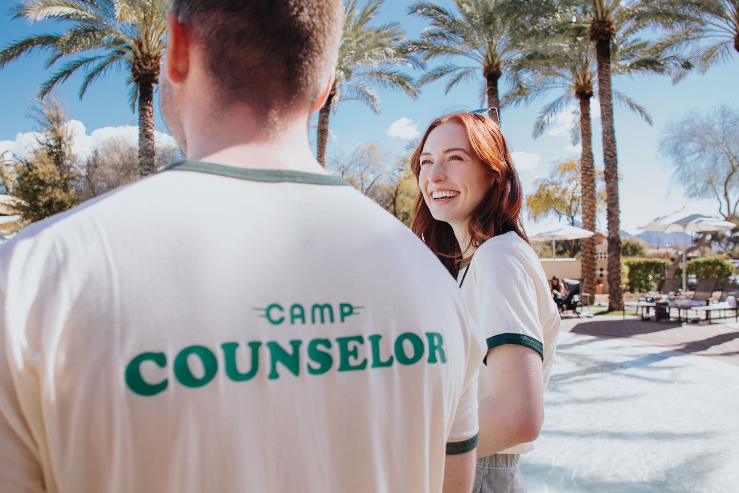 Camp counselors in uniform shirts gathered outdoors near palm trees.