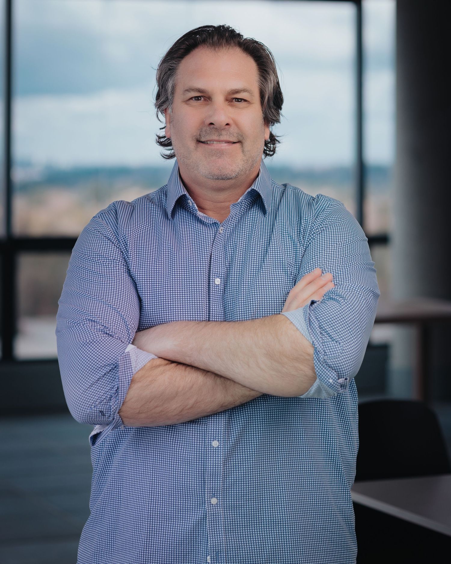 Professional portrait of someone in a blue button-down shirt against a dark background.