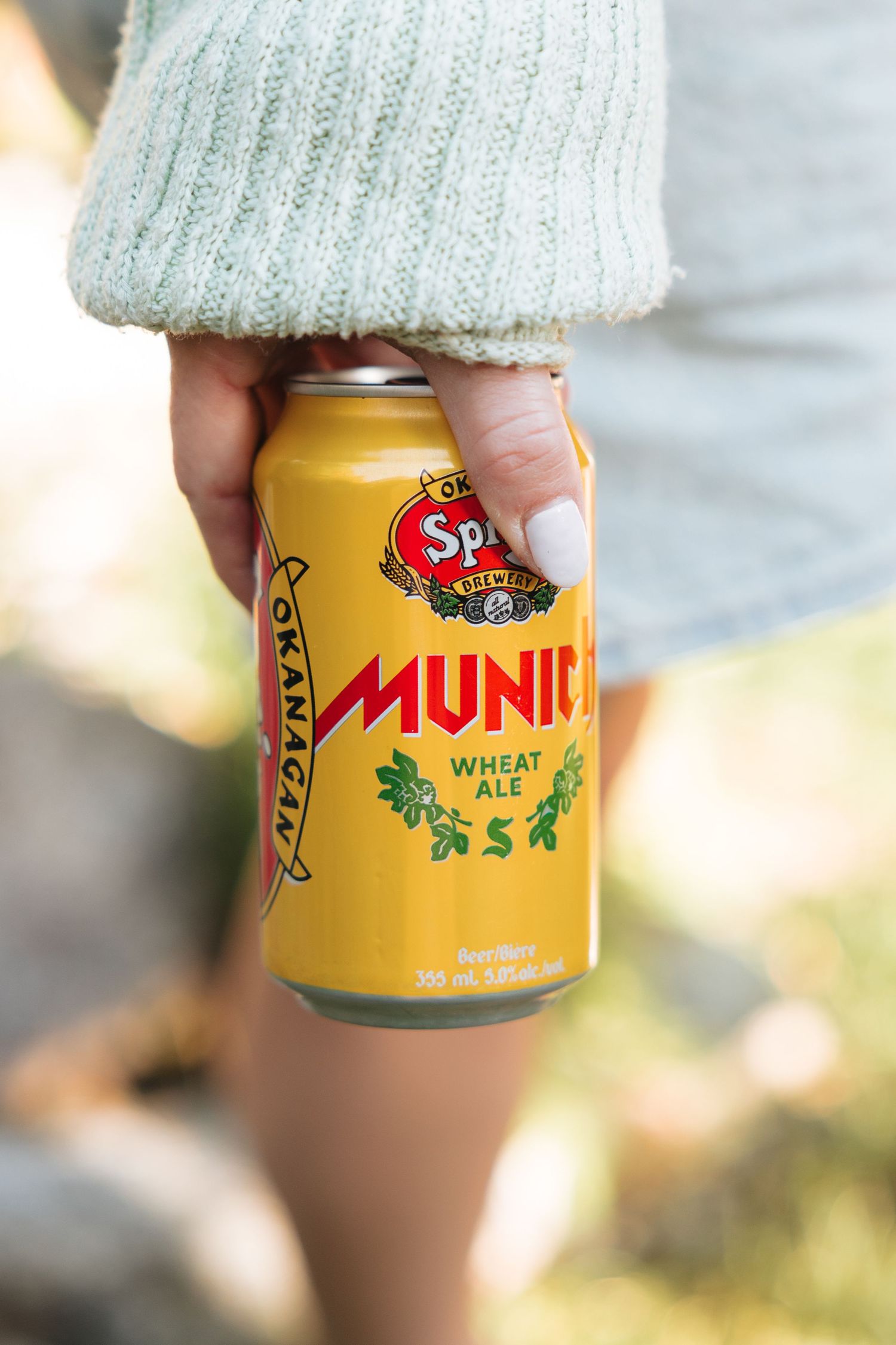 Yellow Spring Valley Munic wheat ale can held against mint green knit sweater.