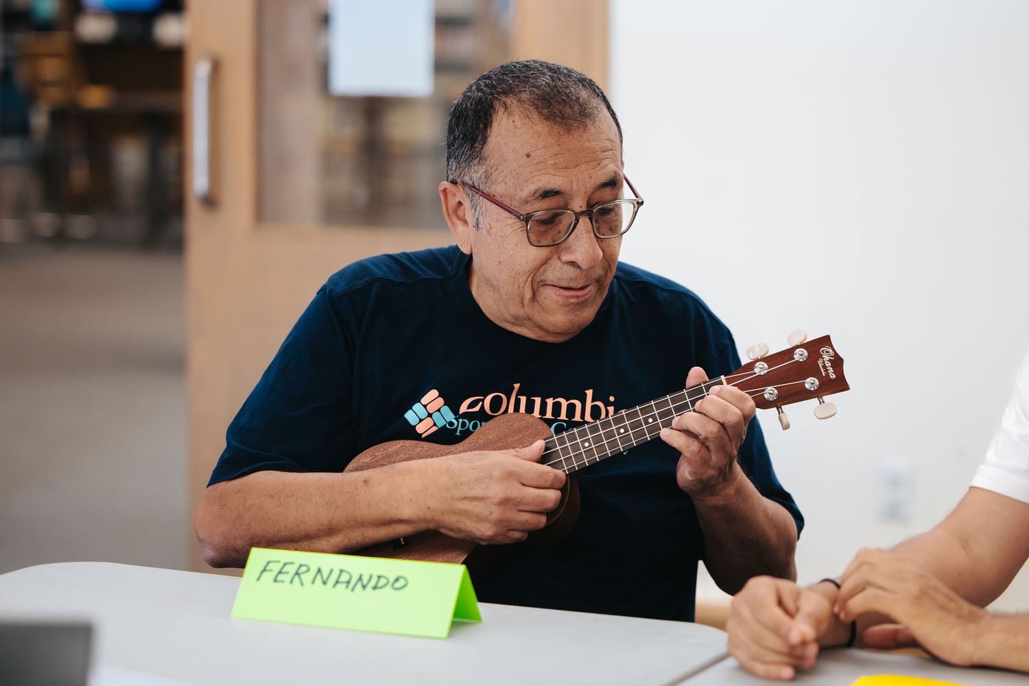 Person in glasses playing ukulele during an indoor activity session.