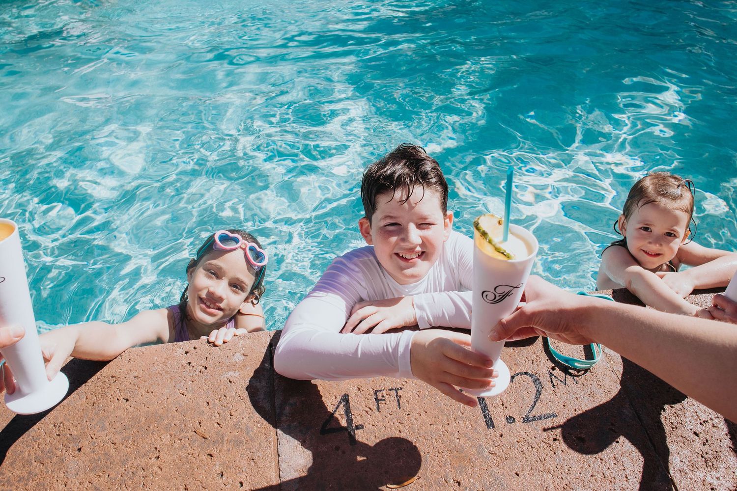 Children and counselors playing together at the edge of a bright blue swimming pool.