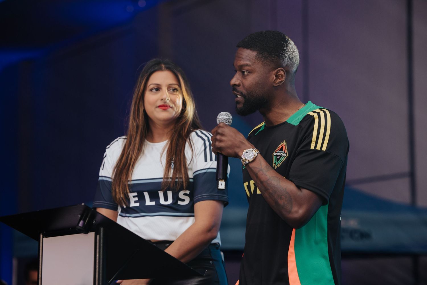 Presenters on stage during an esports or gaming event with blue lighting effects.
