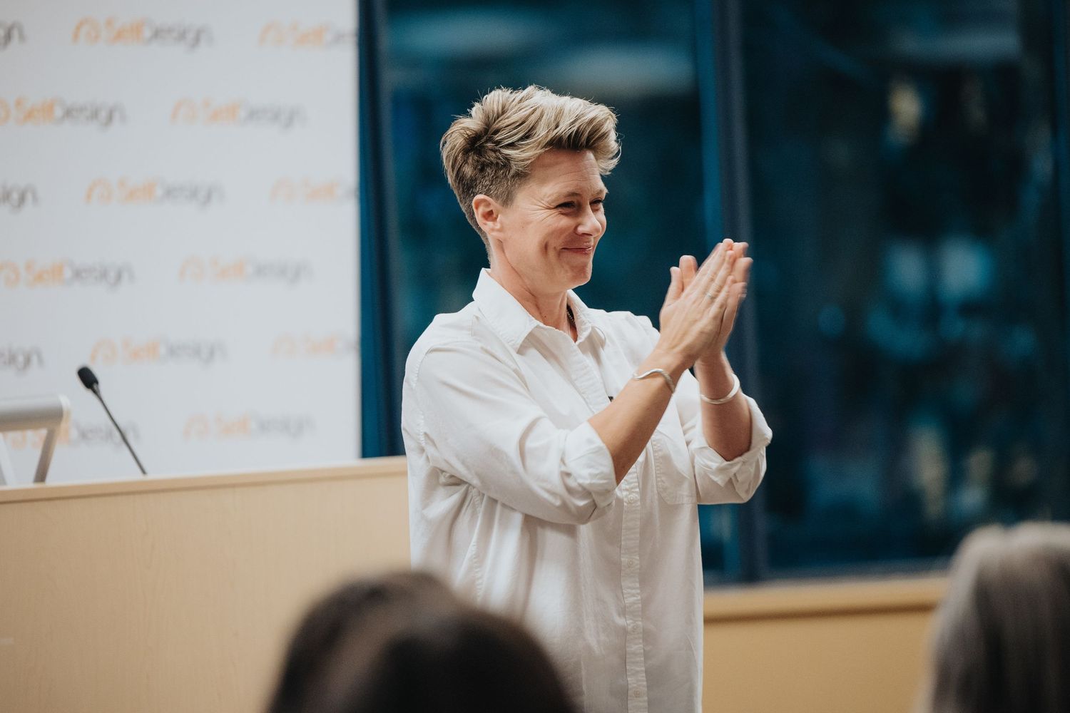 A presenter in a white shirt applauds while standing in front of a whiteboard during a business presentation.