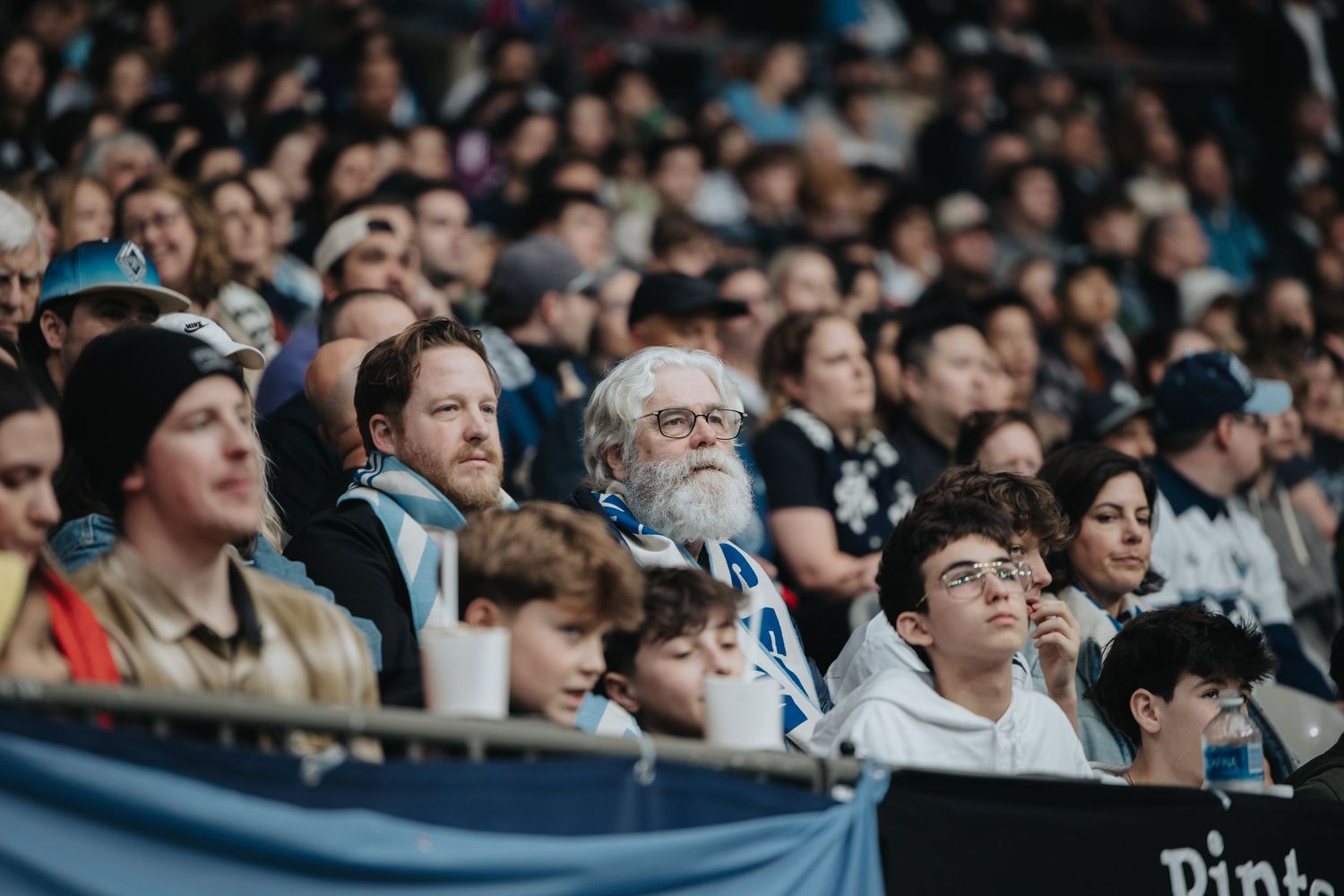 Crowd of spectators intently watching a sporting event in stadium seating.