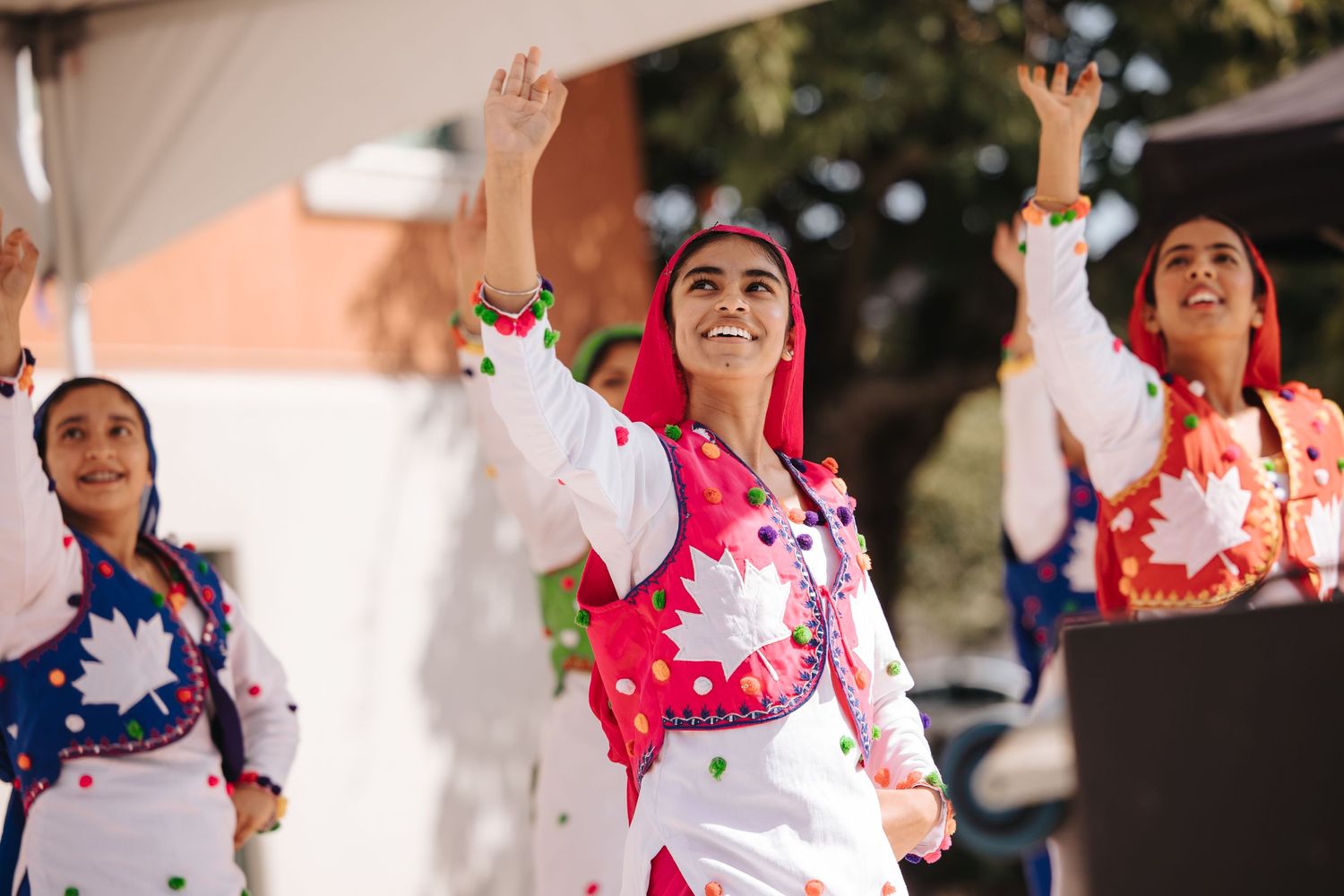 Dancers in colorful traditional outfits performing with raised arms under a tent.